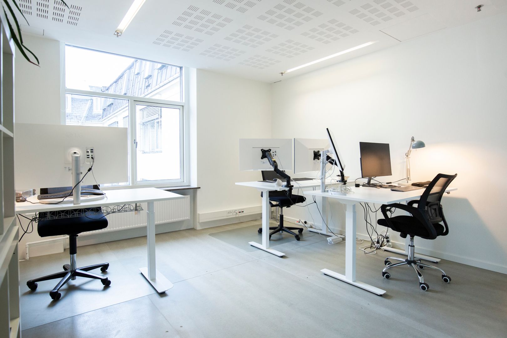 Kontor med høje hvide vægge, højteknologiske skriveborde og højkvalitets ergonomiske stole og to skærme samt en lysestage