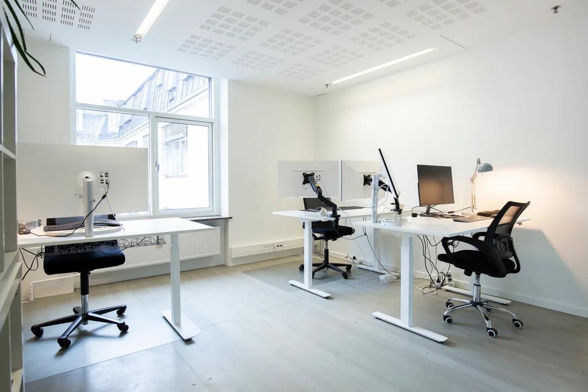 Kontor med høje hvide vægge, højteknologiske skriveborde og højkvalitets ergonomiske stole og to skærme samt en lysestage