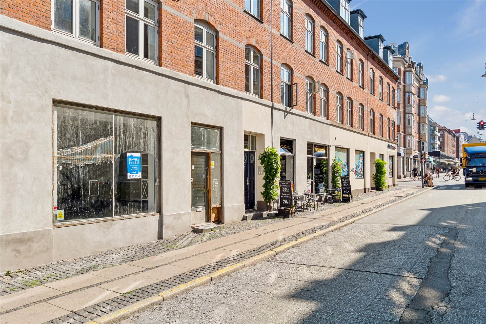 En tom erhvervslejemål på Valby Langgade med udsigt til gaden og terrasse med stole og borde udenfor