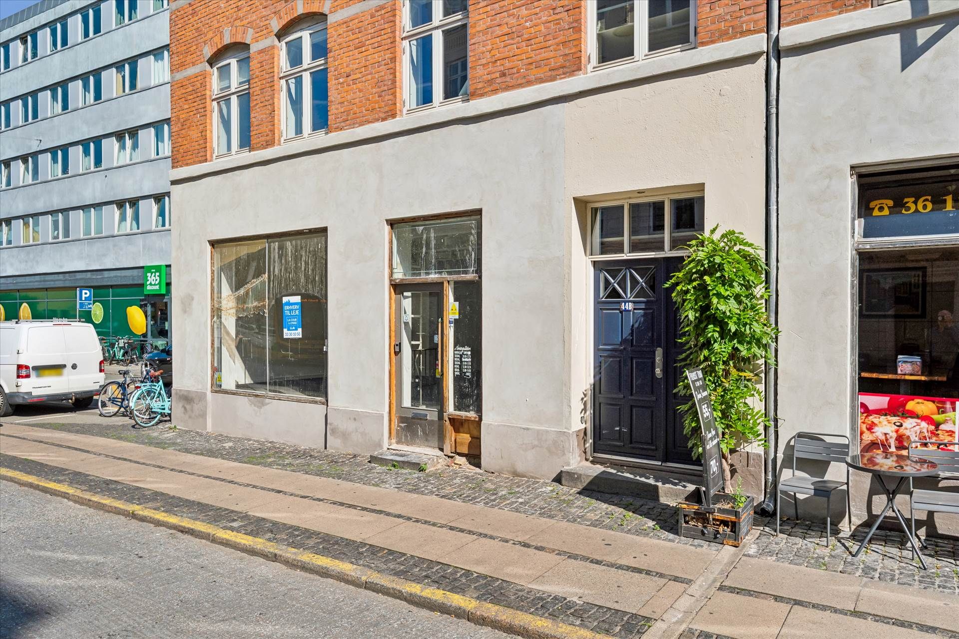 En lejlighed med glasvinduer og to indgange til Valby Langgade med en terrasse med bord og stole og en plante i kasse