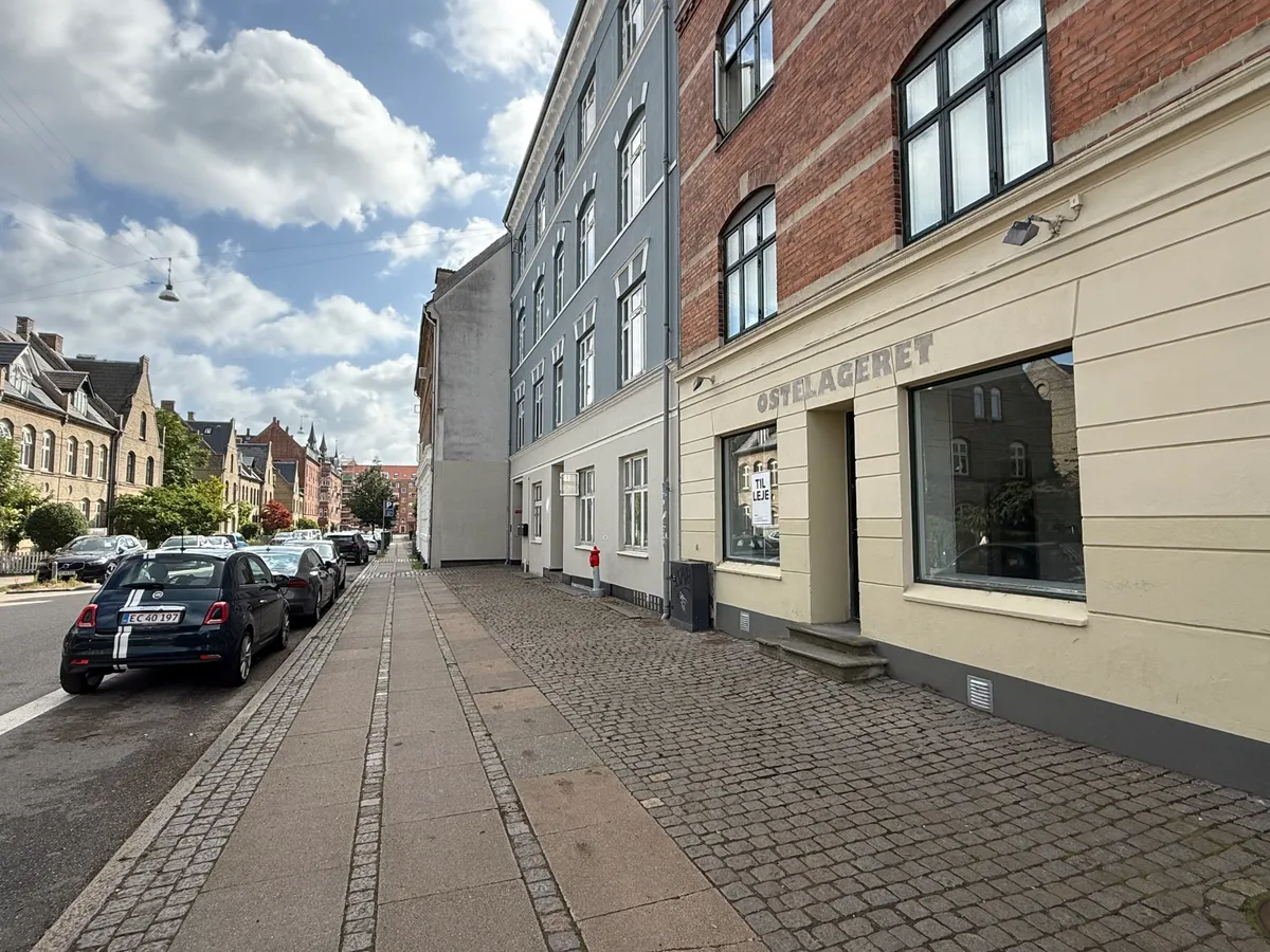 Ostelageret skriver på facaden, og biler er parkeret langs siden af gaden