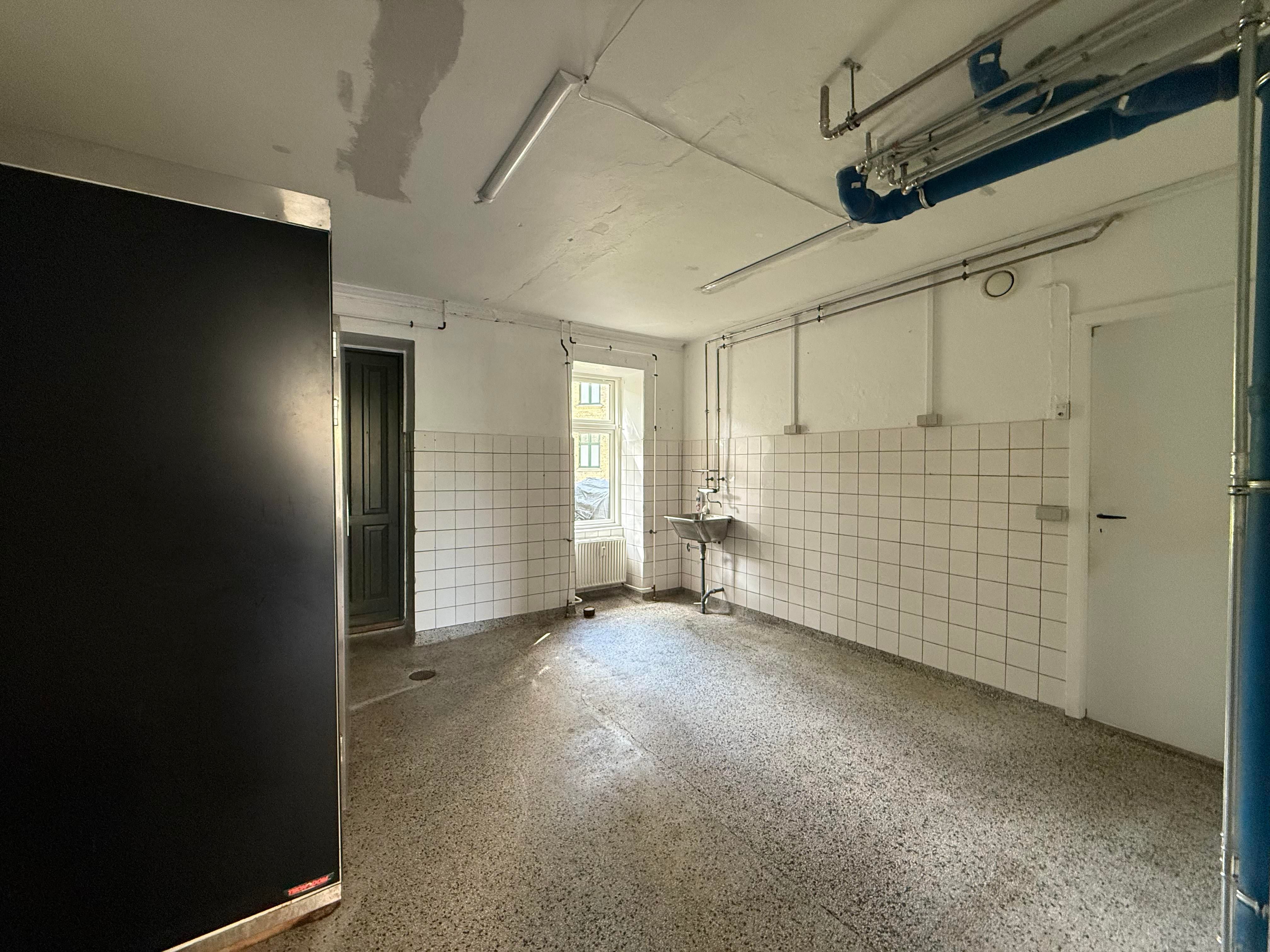 Et tomt lokale med hvide vægge, en metallisk dør og en radiator, en skab og et vindue i rummet