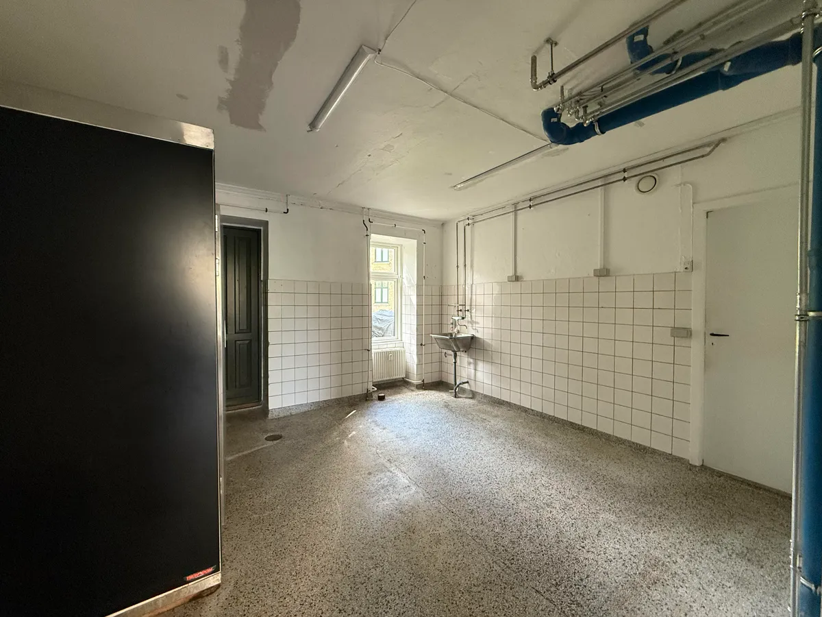 Et tomt lokale med hvide vægge, en metallisk dør og en radiator, en skab og et vindue i rummet