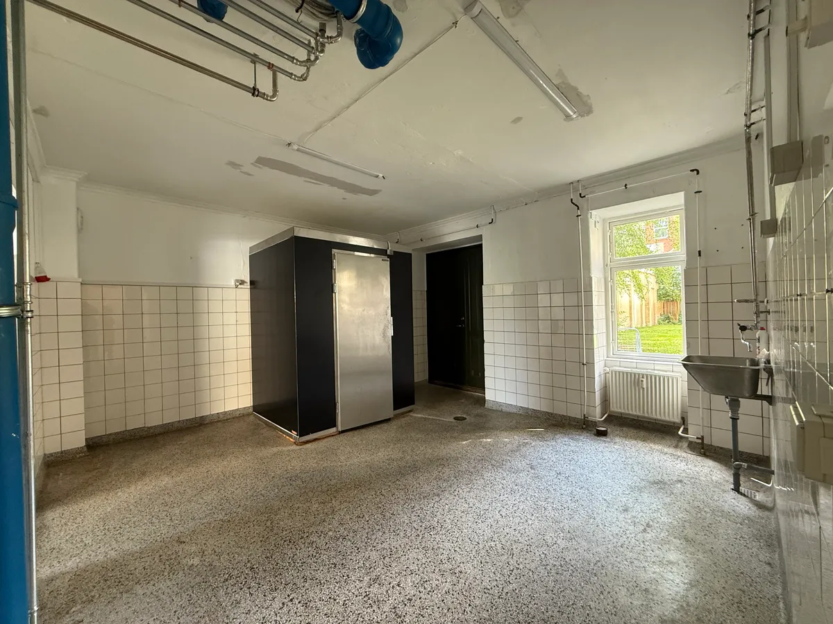 Store, rummelige lokaler med vinduer og radiatorer. Der er et køleskab og et badeværelse med et trægulv.