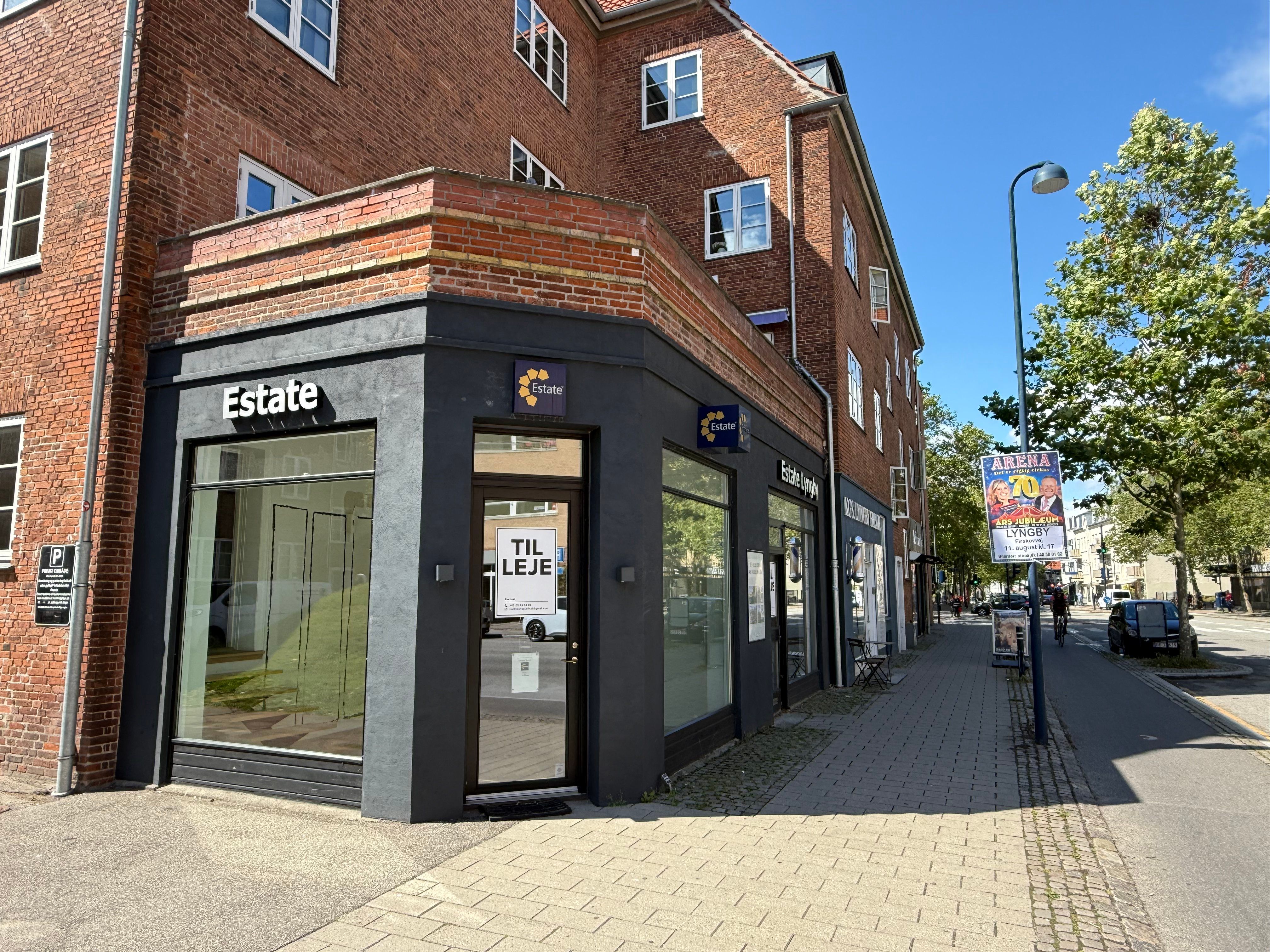 En ejendomsmæglerkontor Estate tilbyder erhvervslejemål i en rødmalet bygning med glasvinduer og stående skilte