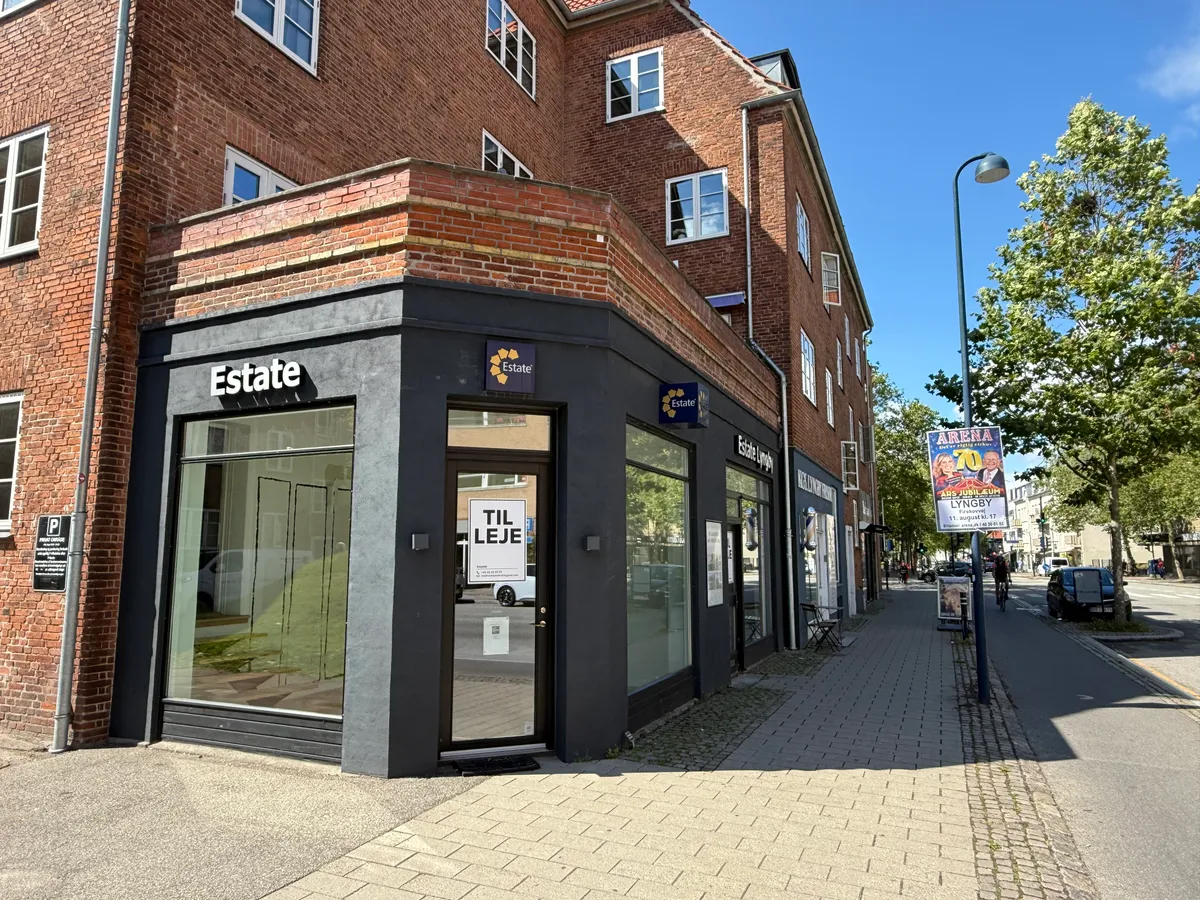 En ejendomsmæglerkontor Estate tilbyder erhvervslejemål i en rødmalet bygning med glasvinduer og stående skilte