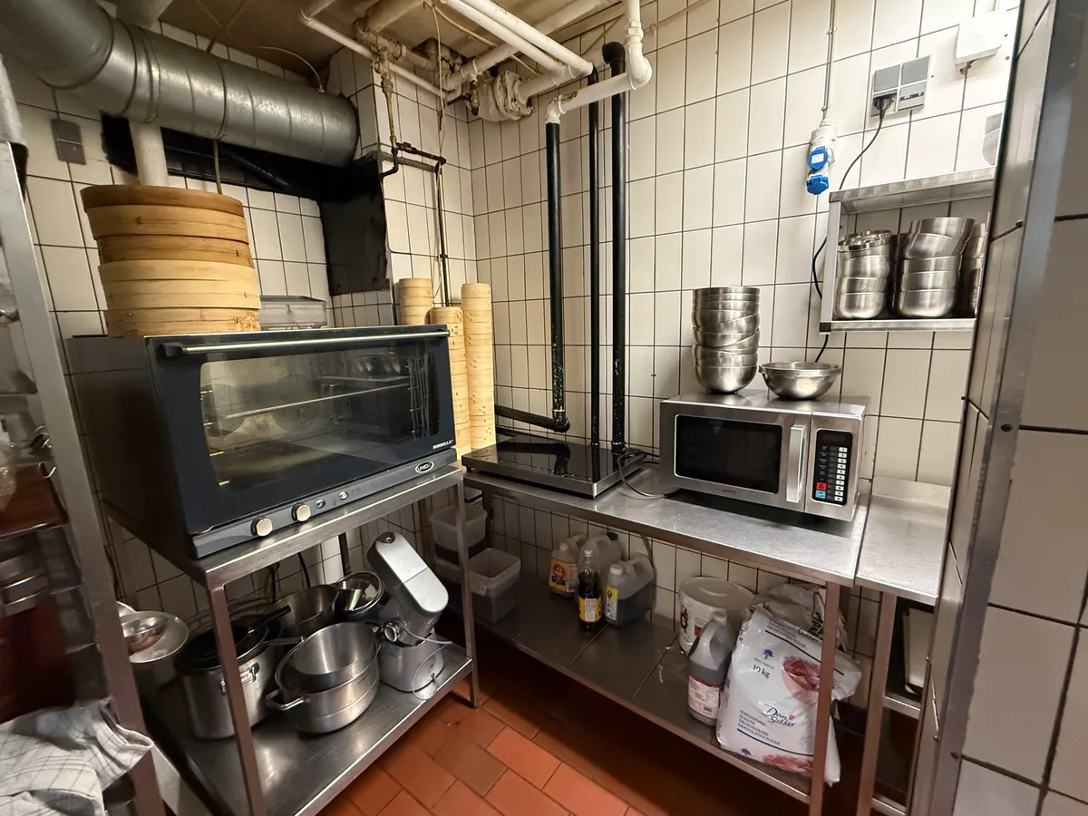 Køkken med komfuret, ovnen, mikrobølgeovnen, flere beholdere, bønner og flasker samt en række metalborde med køkkenudstyr