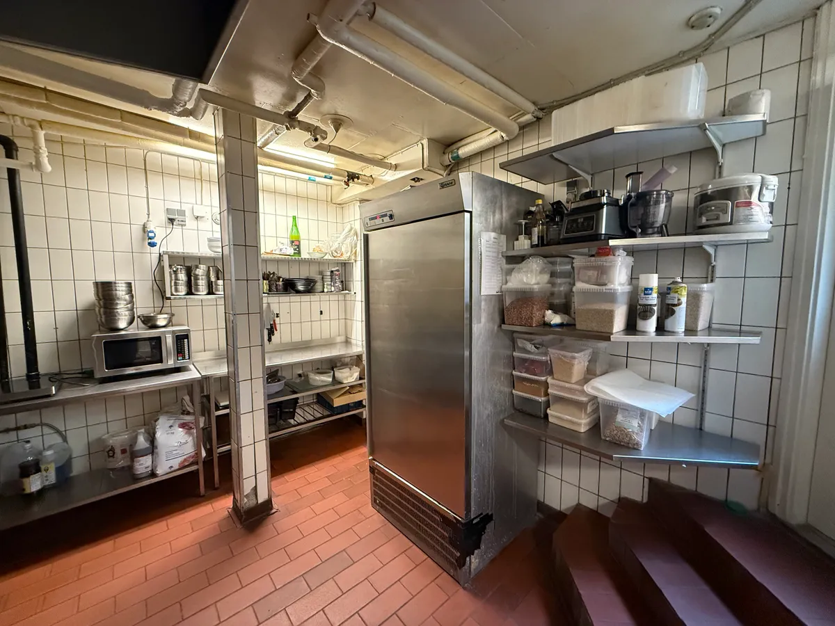 Indkøbsvogne, tønde, gryder og flasker i et køkken med en mikrobølgeovn og en fryser i baggrunden og en trappe til siden