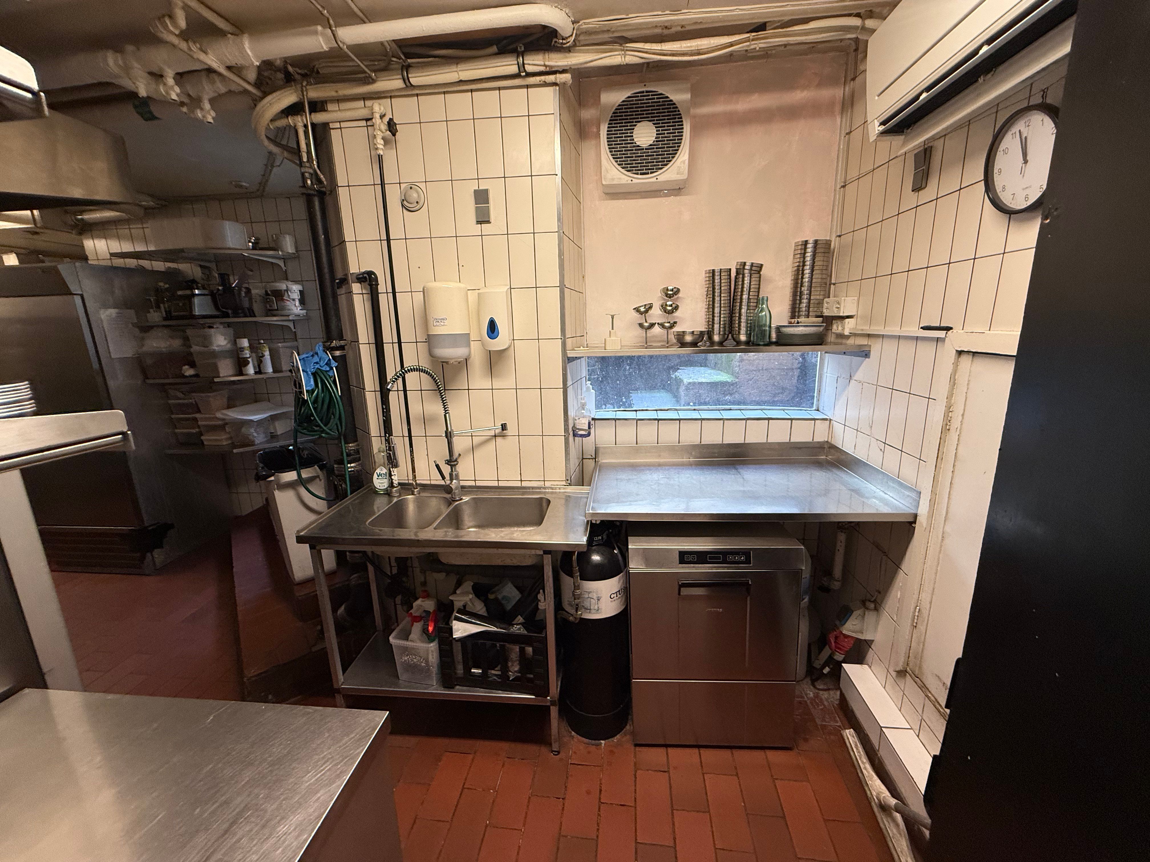 Køkken med dobbelt vask, ventiler, køleskab, kælder, luftpumpe og klokeskilt på væggen