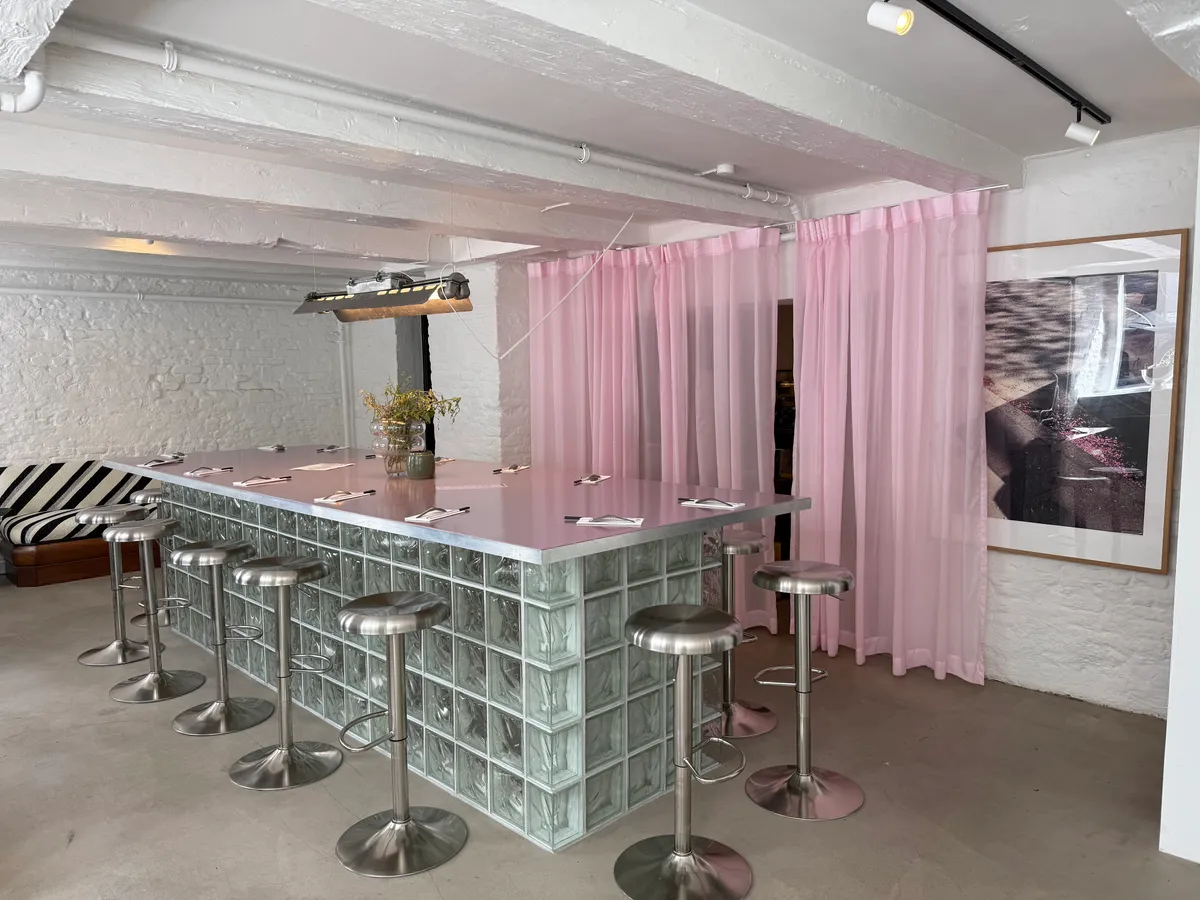 En stor glas og stål bar med en vase og planter samt flere høje stole og et billede i ramme på væggen