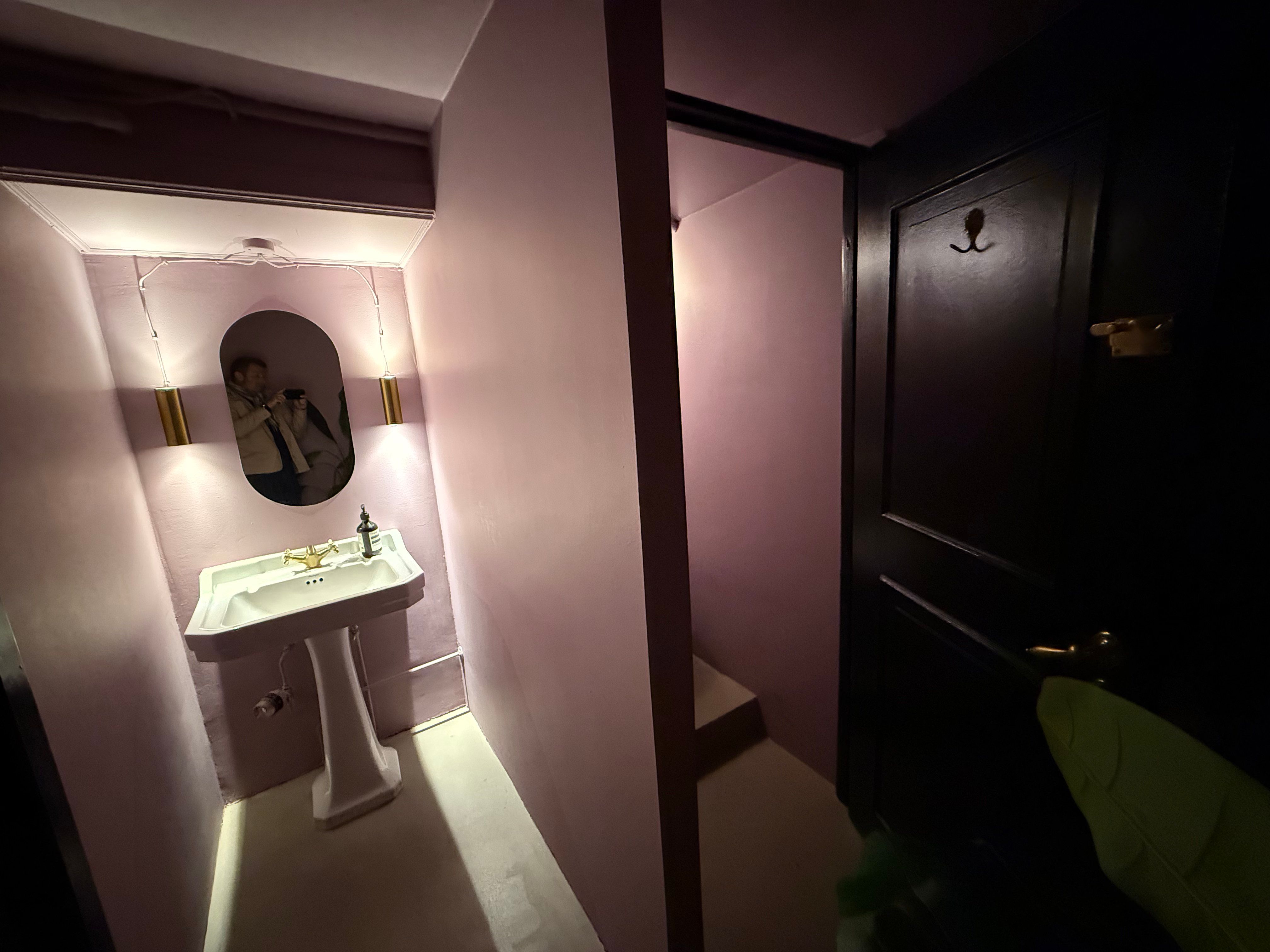 Lyserødt badeværelse med højt loft og stort spejl og hvid vask og lysekroner