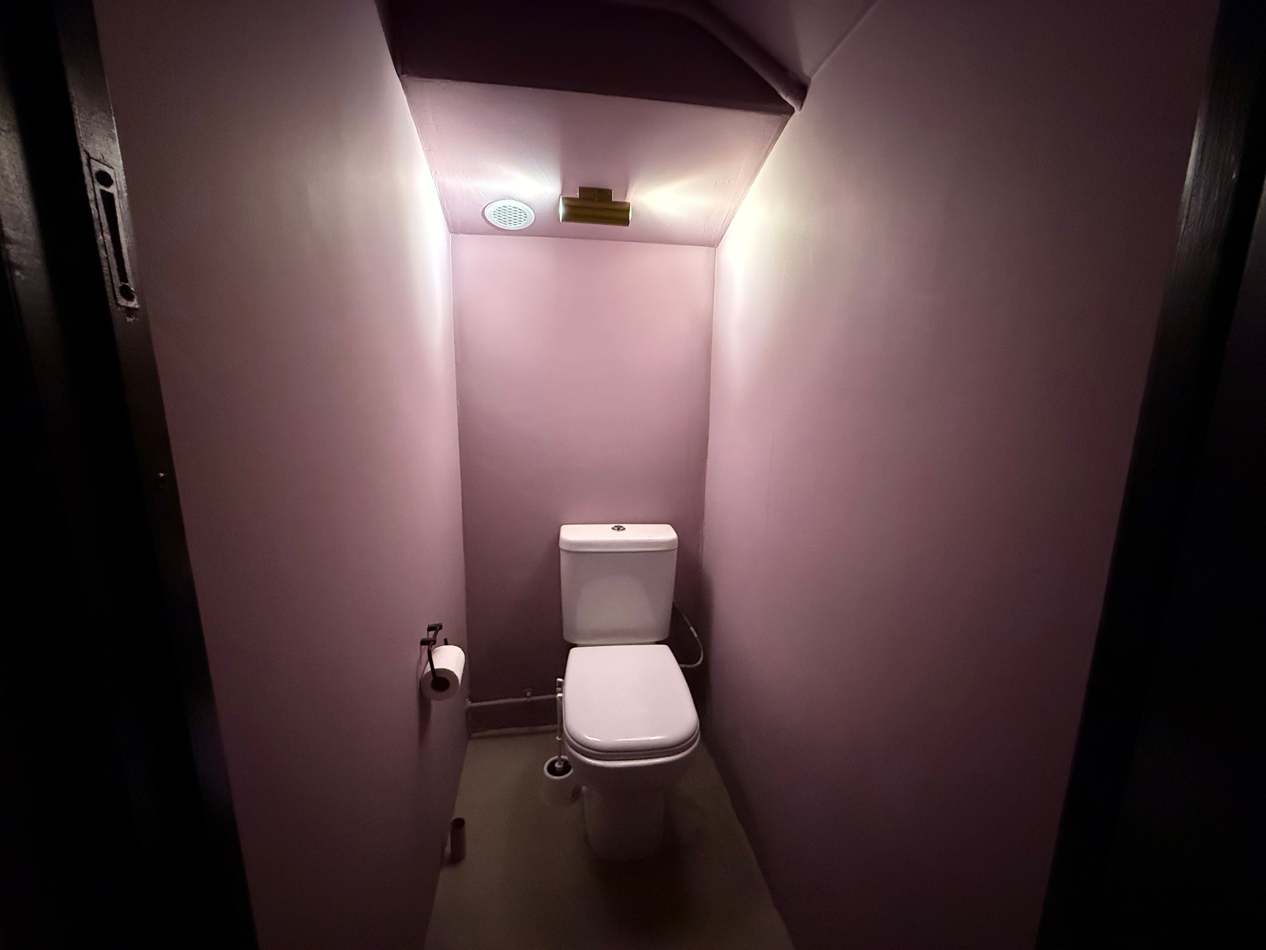 En lille toiletrum med en toilet, en toiletpapirholder og en lysstige på væggen