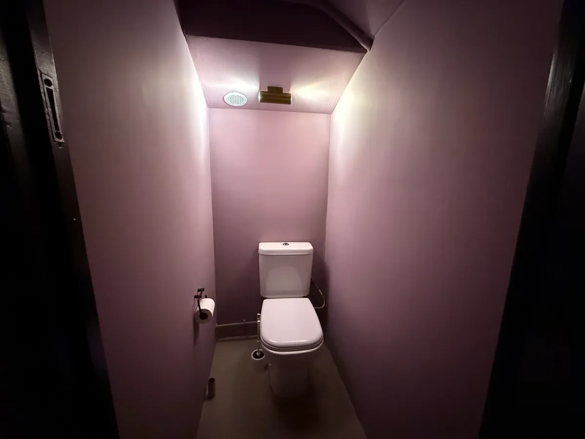 En lille toiletrum med en toilet, en toiletpapirholder og en lysstige på væggen