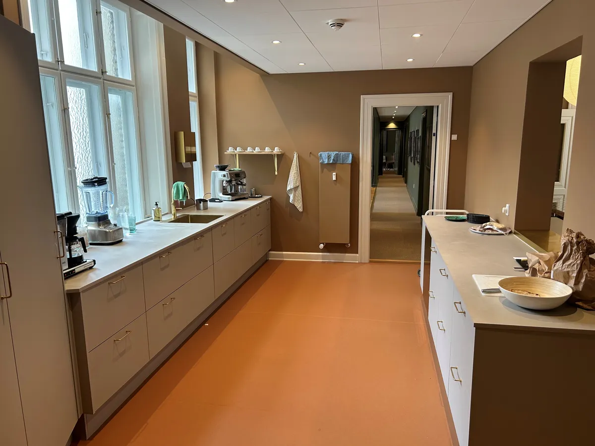 Køkken med moderne møbler, kaffemaskine, blender, gryder og kar, og en åben dør til et andet rum