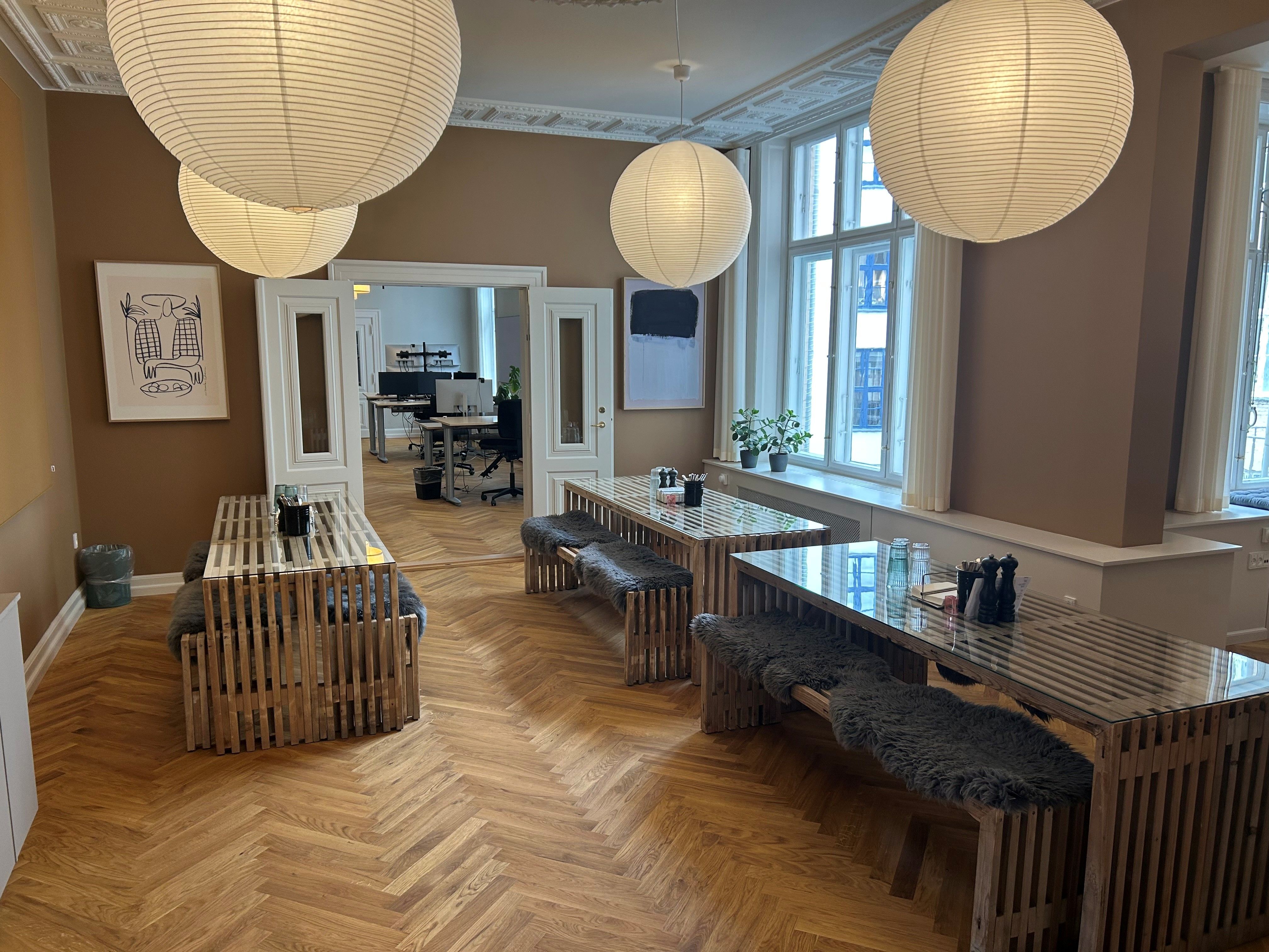 Store papirlys hængende i loftet og lysegule vægge med møbler og stole. Vægmalerier og plantepoteter på vindueskarmen.