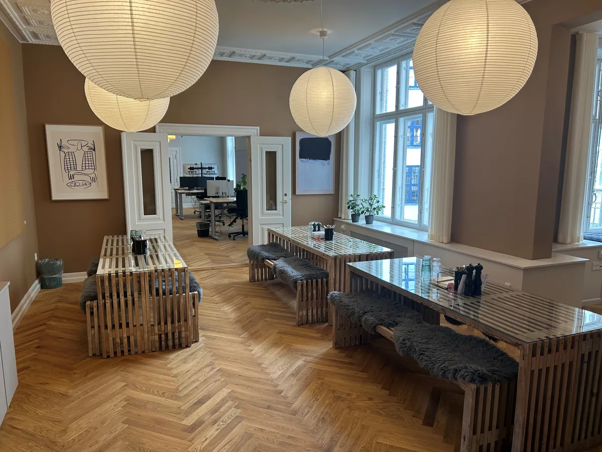 Store papirlys hængende i loftet og lysegule vægge med møbler og stole. Vægmalerier og plantepoteter på vindueskarmen.