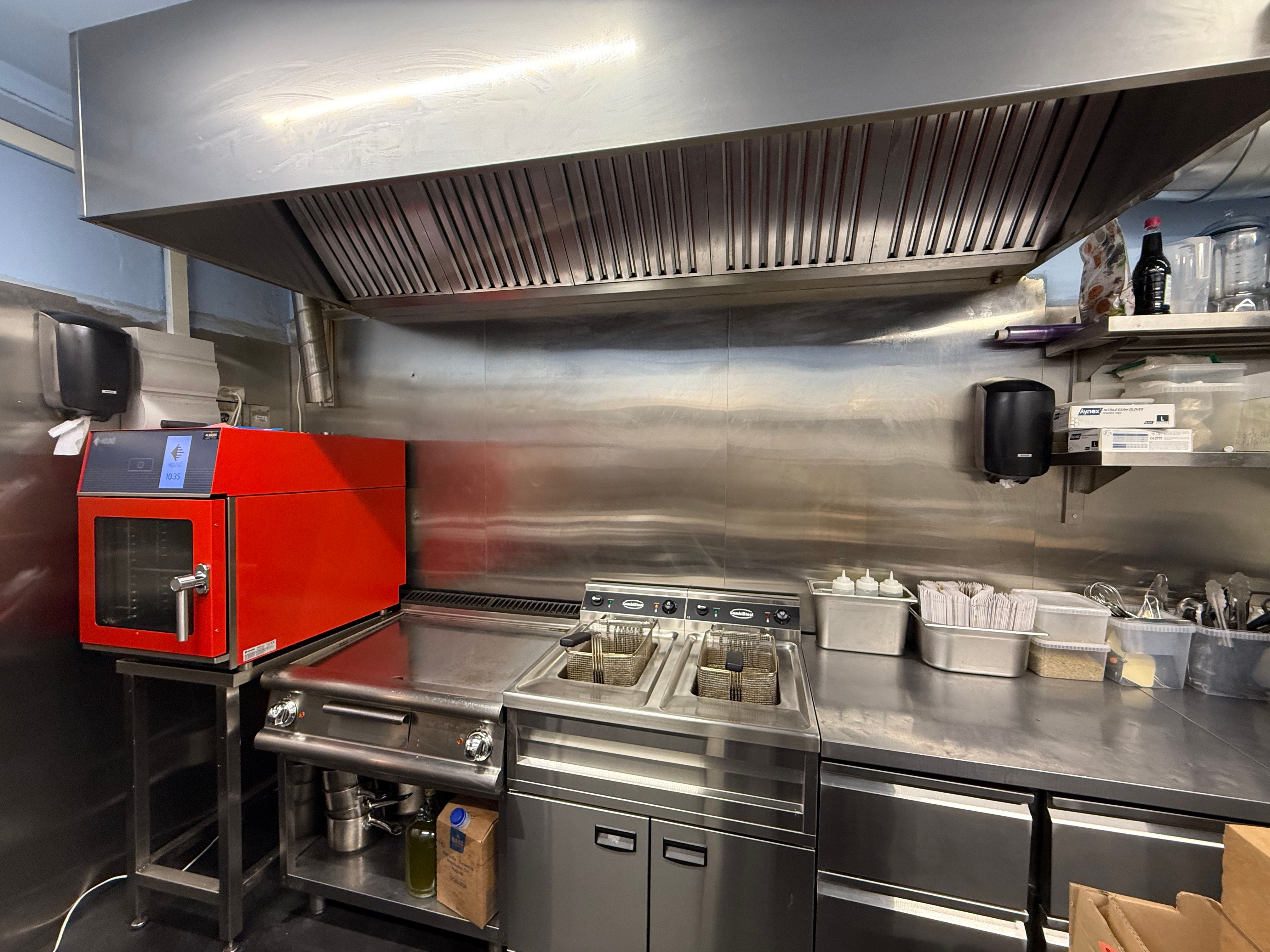 En ren kommerciel køkken med moderne apparater og udstyret med stålborde og -hylder, samt en rød ovn og en kommerciel