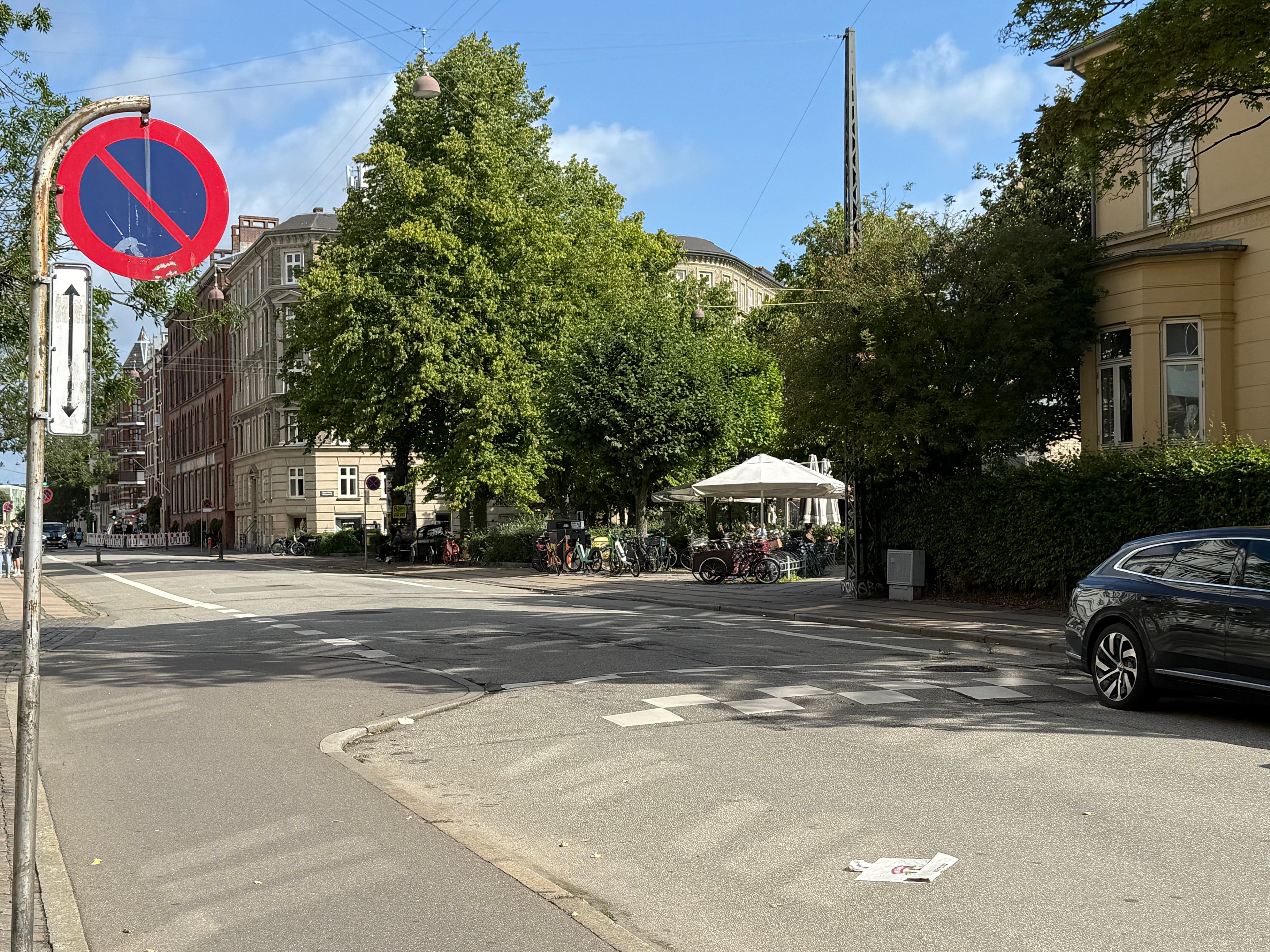 Vejkryds med et parket område, cykler, en bil, gågade og et højhus med udsigt til Bopa Plads på Randersgade 35 på Østerbro