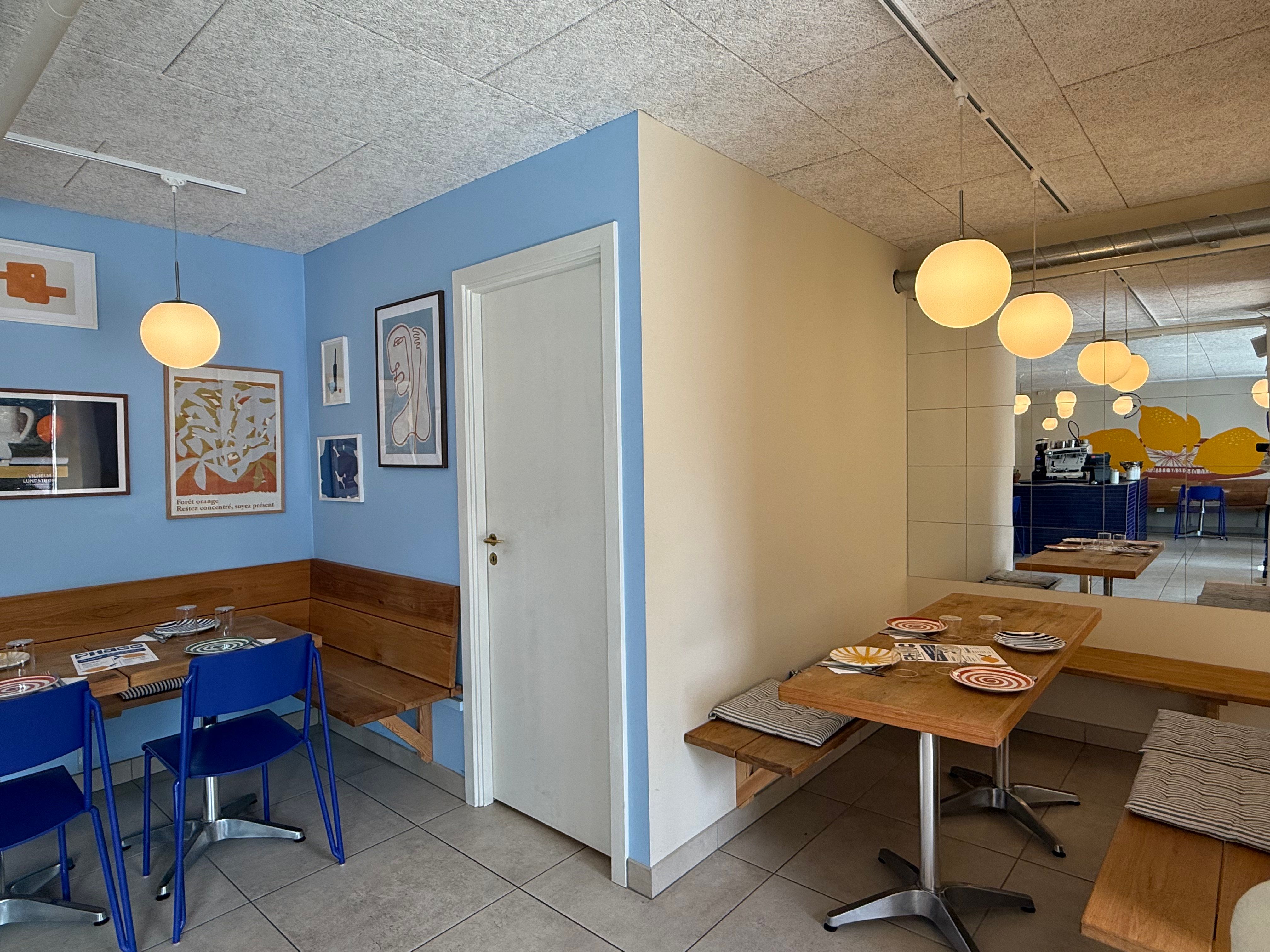 En lille kafe med lyserøde loftslampe, hængende fra loftet, og borde med tallerkener og vinglas