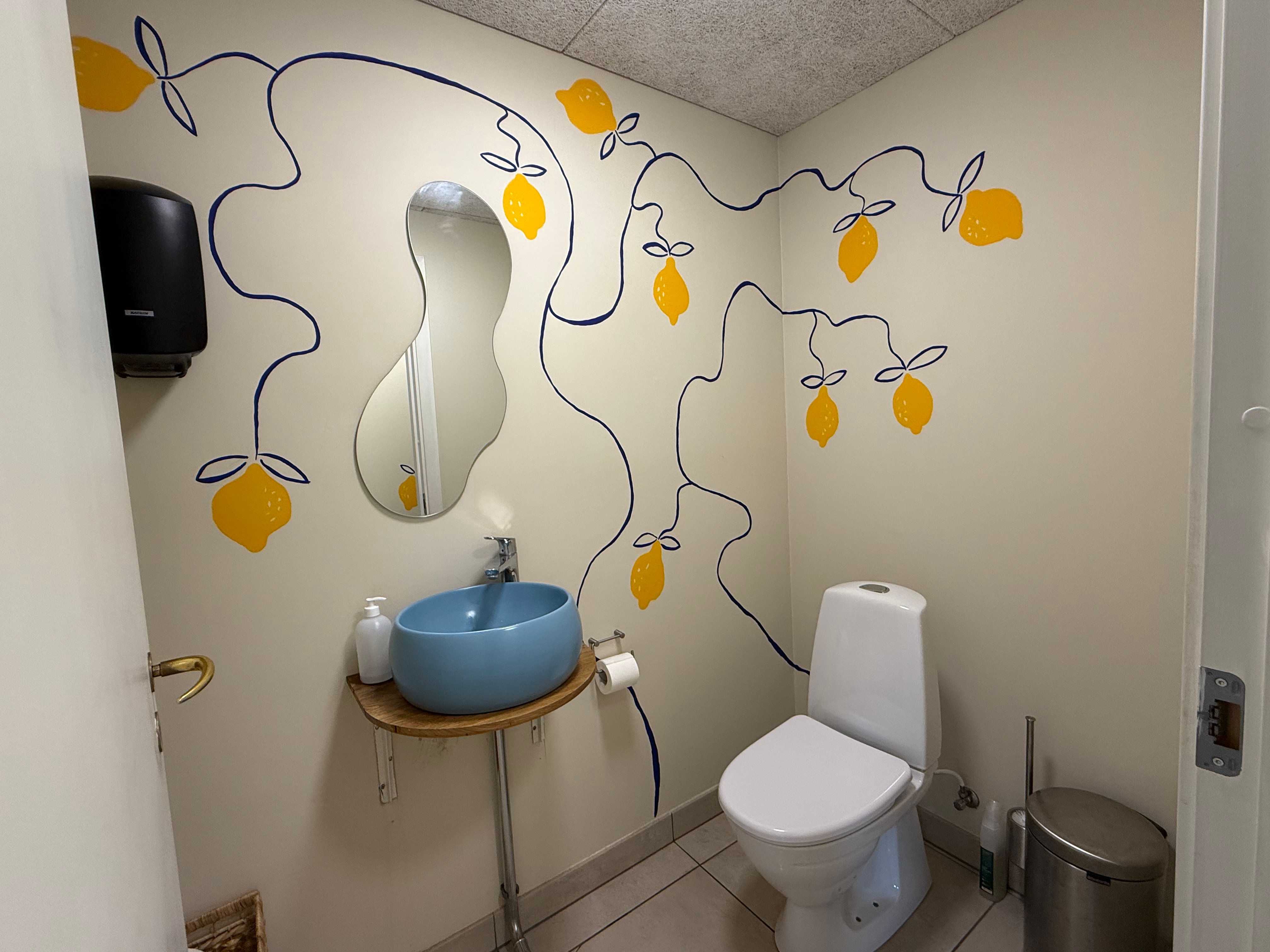 Et lille badeværelse med en rund blå vask, hvidt toilet, en spejl, et toiletpapir og en lukket dør