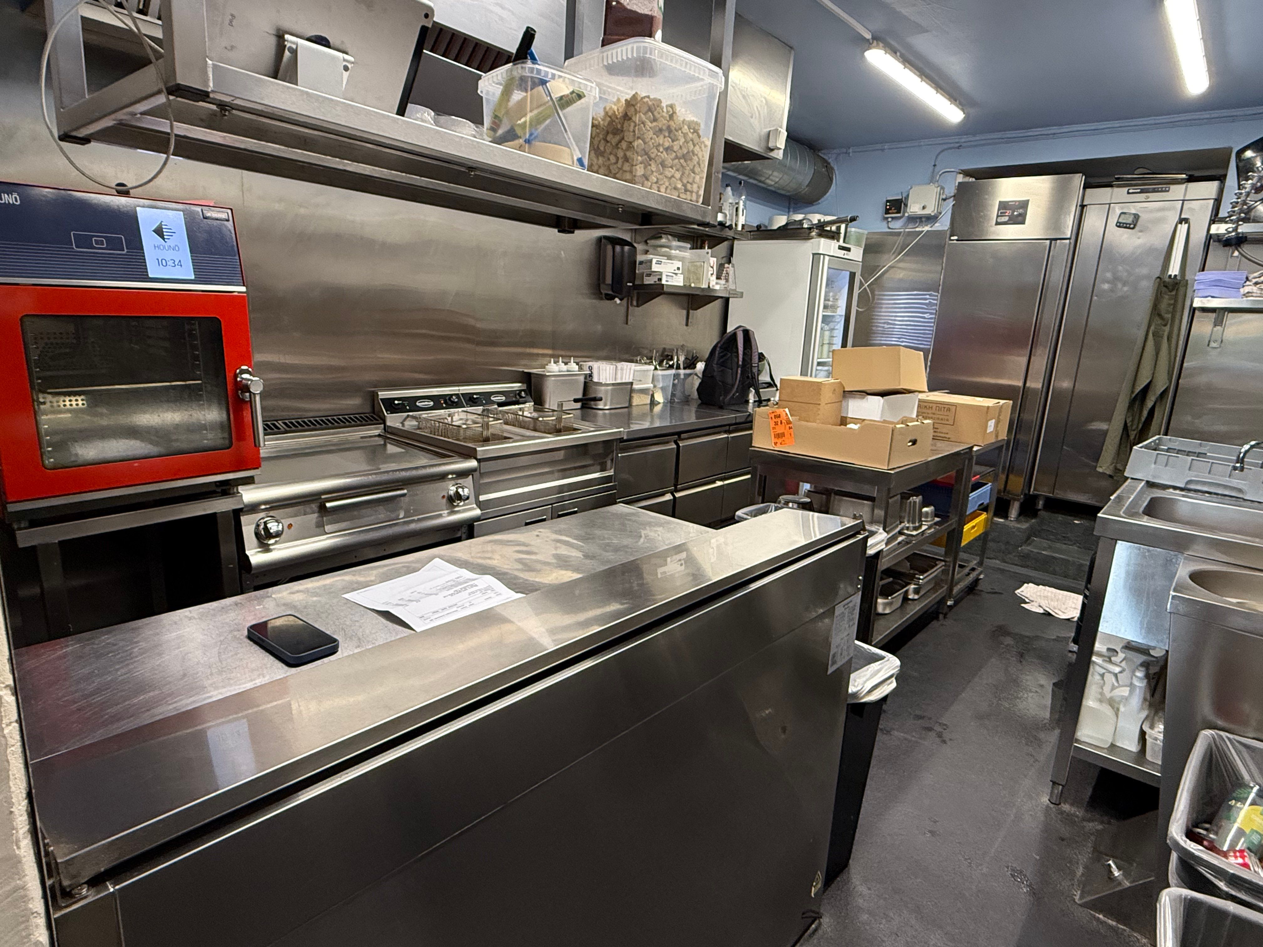 En køkken med moderne apparater og rustfrit stål udstyr, sammen med flere emballagekartoner og et søjlebord.