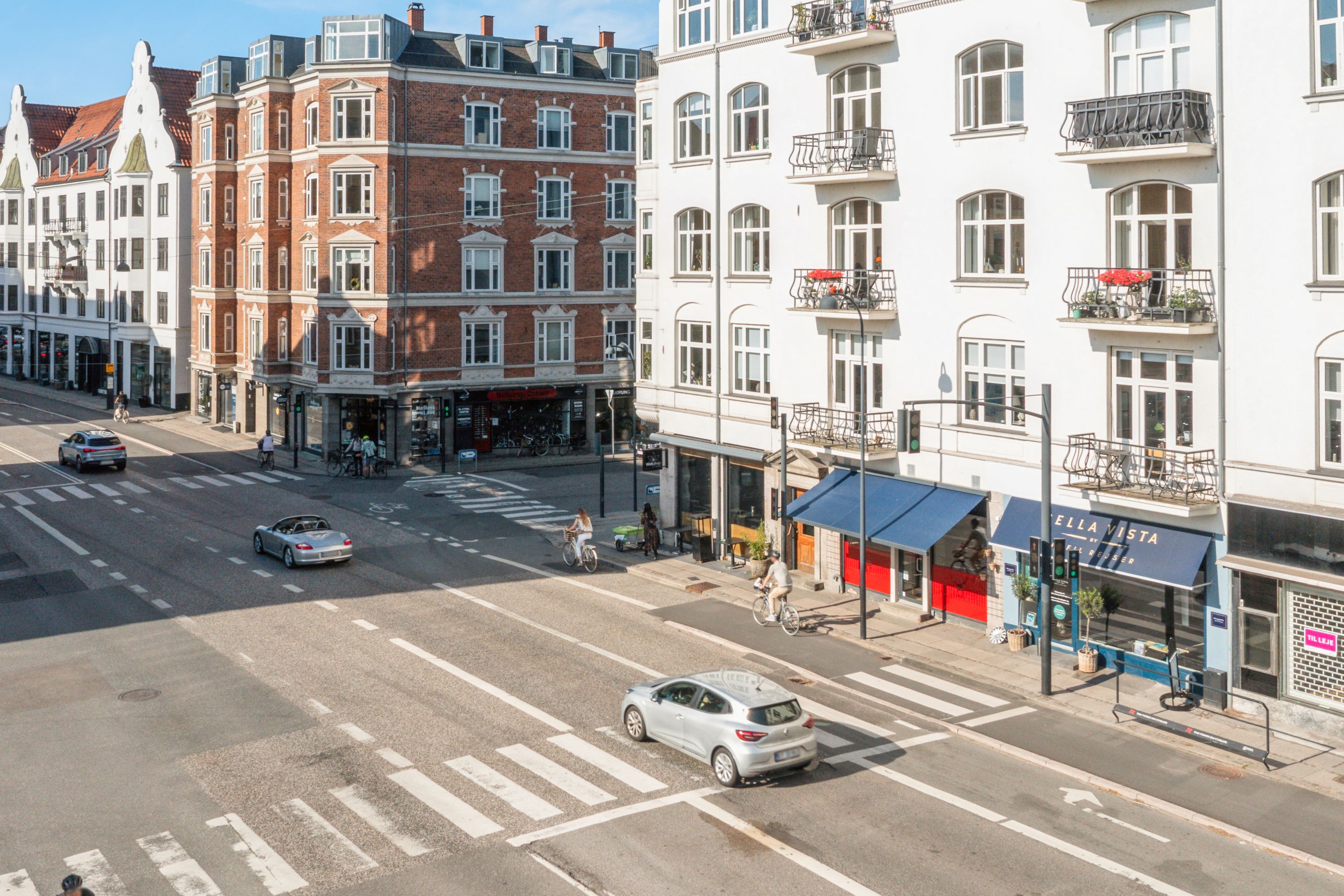 Folk køre med biler og cykler langs Strandvejen i Hellerup med forretninger og gavl til bygninger