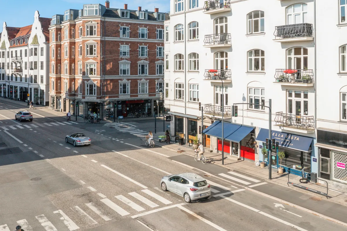 Folk køre med biler og cykler langs Strandvejen i Hellerup med forretninger og gavl til bygninger