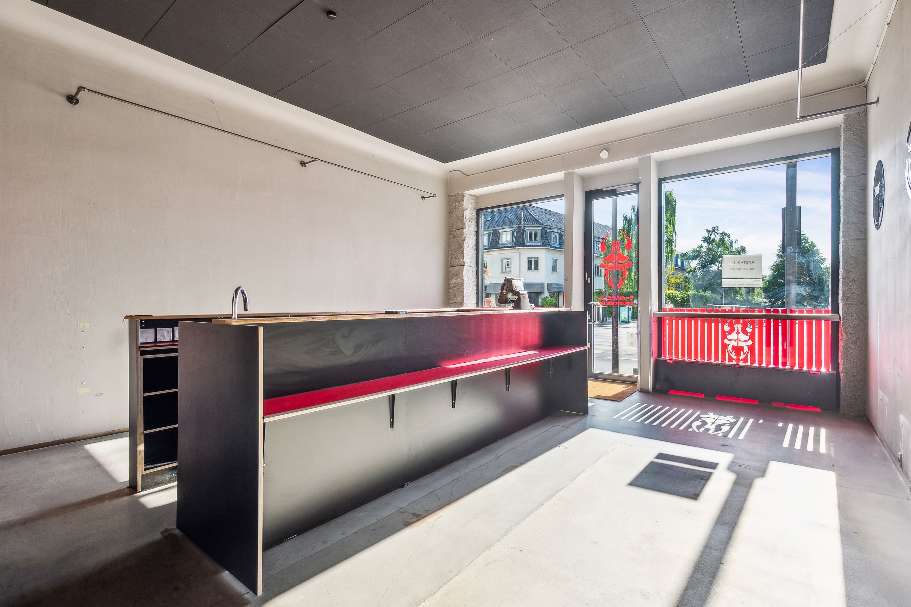 Solsiden på Strandvejen i Hellerup med indgang til restaurant med røde stolpe og rødt mønster på vinduet