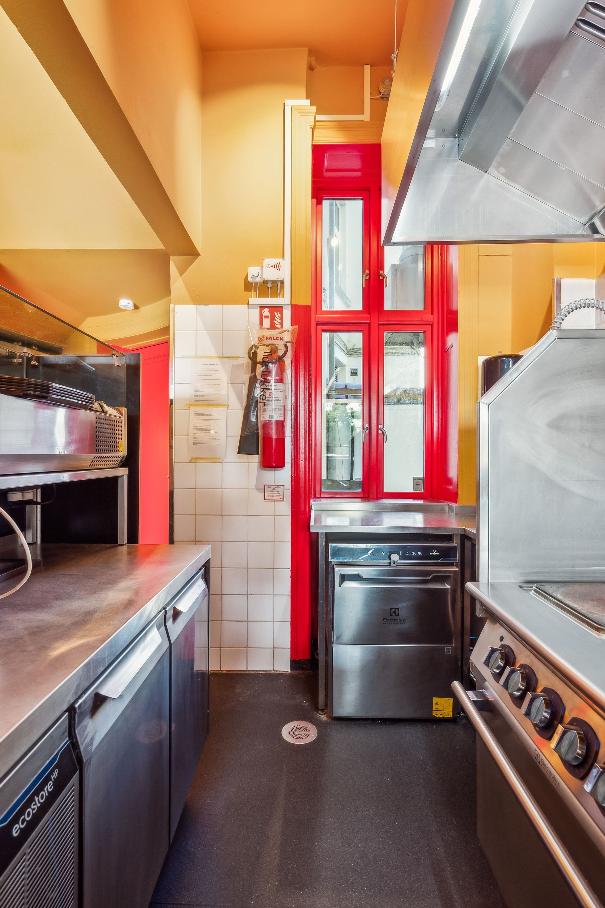 Et moderne køkken med røde ruder og møbleret med flere apparater som ovne, ovn, køleskab og stålbord