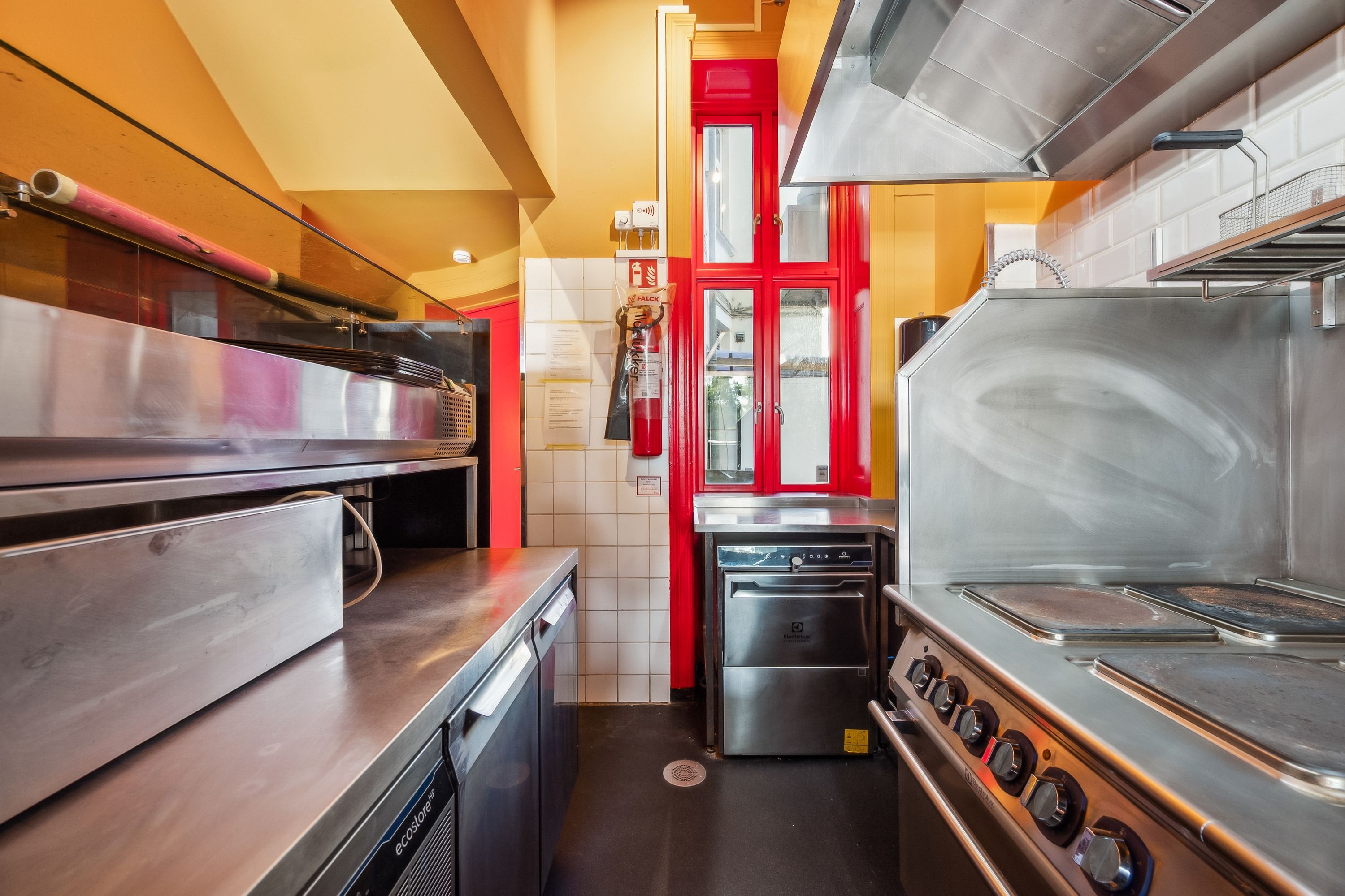 Røgsuger over gaskomfur, ovn og vaskemaskine i en moderne kommerciel køkken med gul gulv og hvide fliser