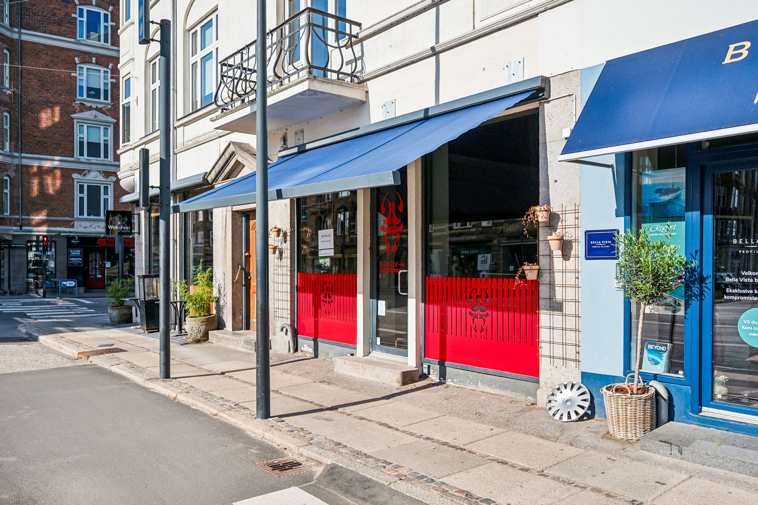 To forretninger med blå aubrægger og røde døre. En med teksten B og den anden med Bella Vista. Mange planter og