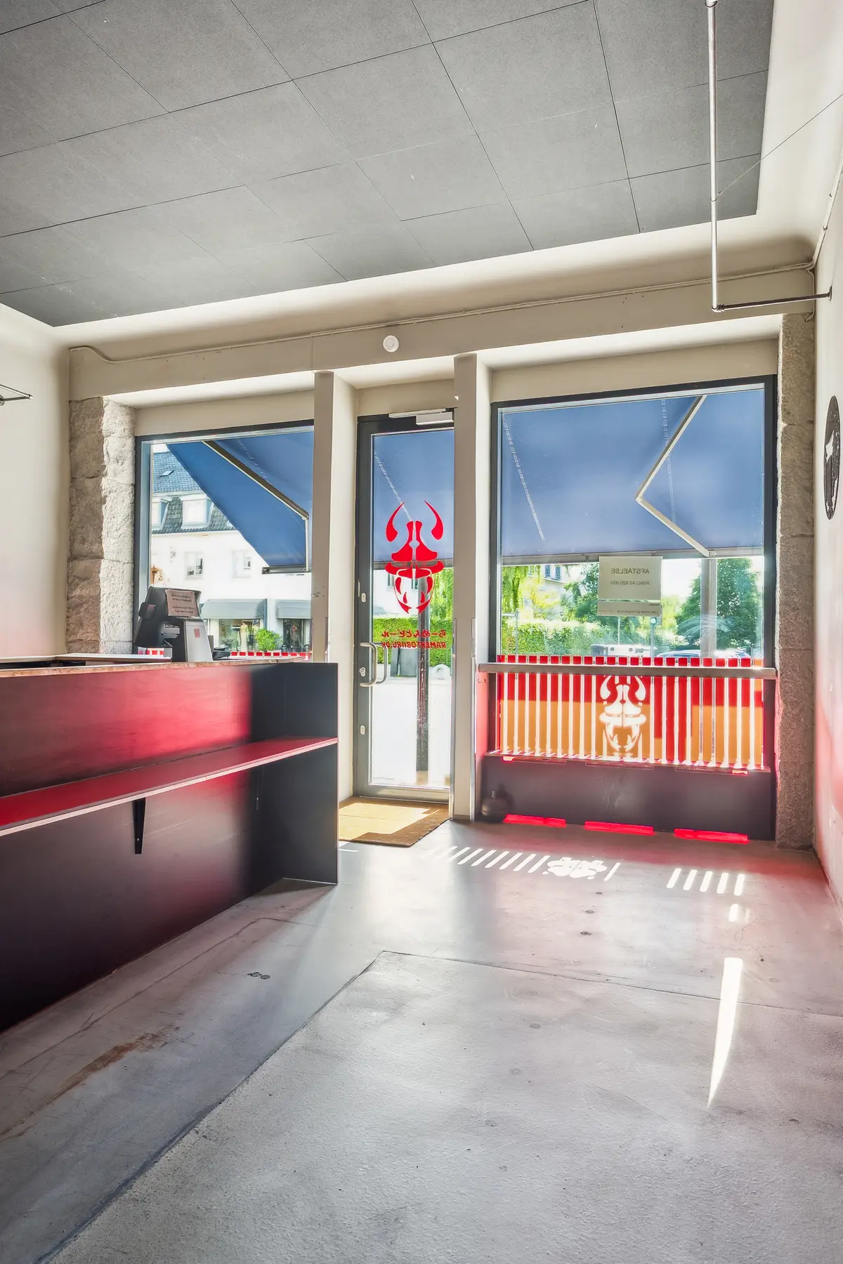 En moderne indgangszone med røde bænke og et rødt mærke på glasdøren og vinduet. Der er en sort gulv og et hvidt loft.