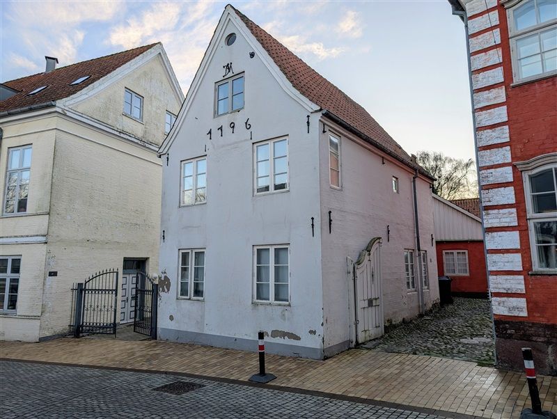 Gårdsplads med tre bygninger og stenbelagt gade og vejside med røde og hvide stribede mursten