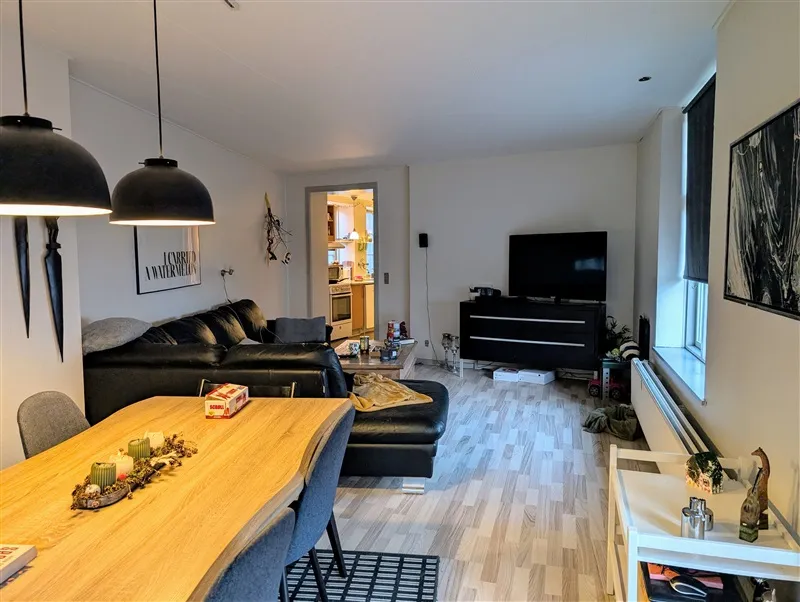 Lejlighed i Aabenraa med moderne møbler, sofa, bord, tv, lysekroner og køkken i baggrunden