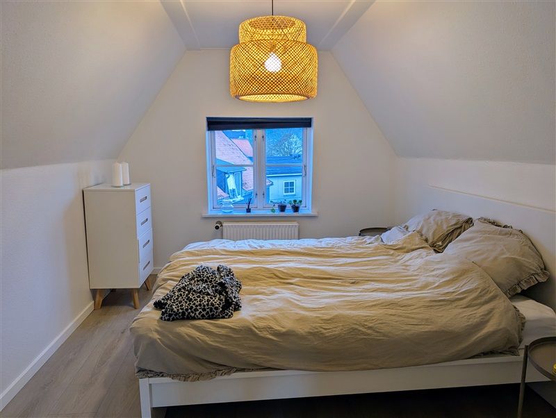 Soveværelse med hvid sengelinned og trægulv samt hyggeligt gult loftslampe og smukke udsigt til byen udenfor vinduet