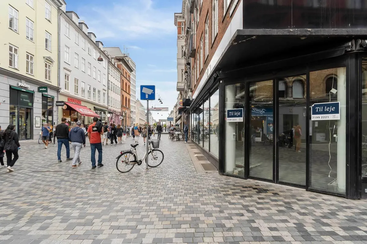 Frederiksborggade er en travl gågade med krydsende gående mennesker og en parkeret cykel i nærheden af en stor butik med