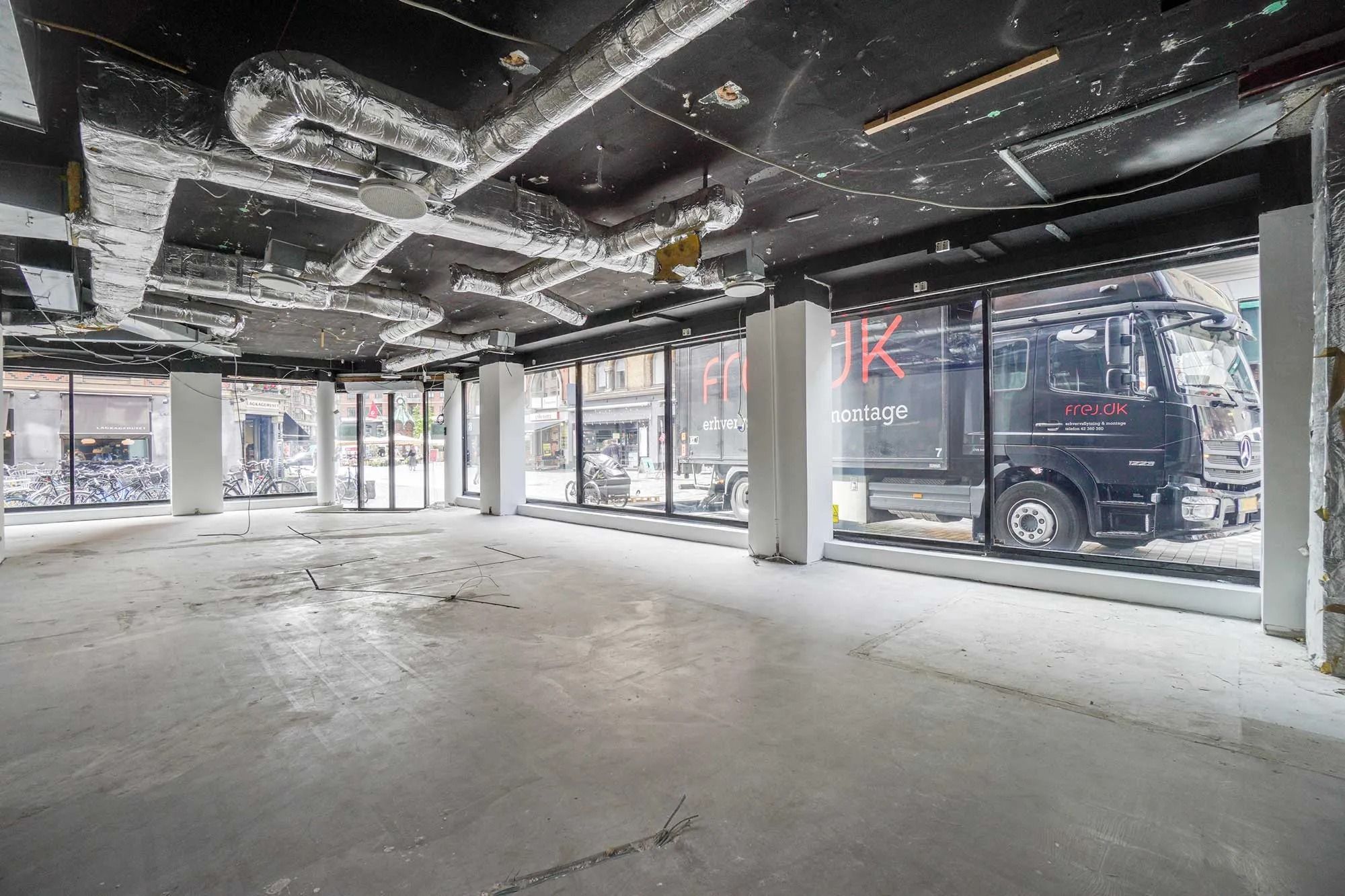 Butik med stort vindue og store, lyse vinduer, hvor der er parkerede cykler og biler udenfor