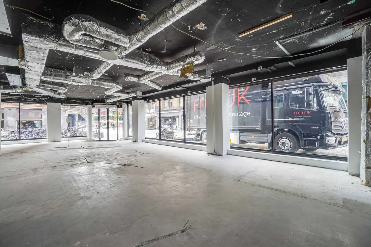 Butik med stort vindue og store, lyse vinduer, hvor der er parkerede cykler og biler udenfor