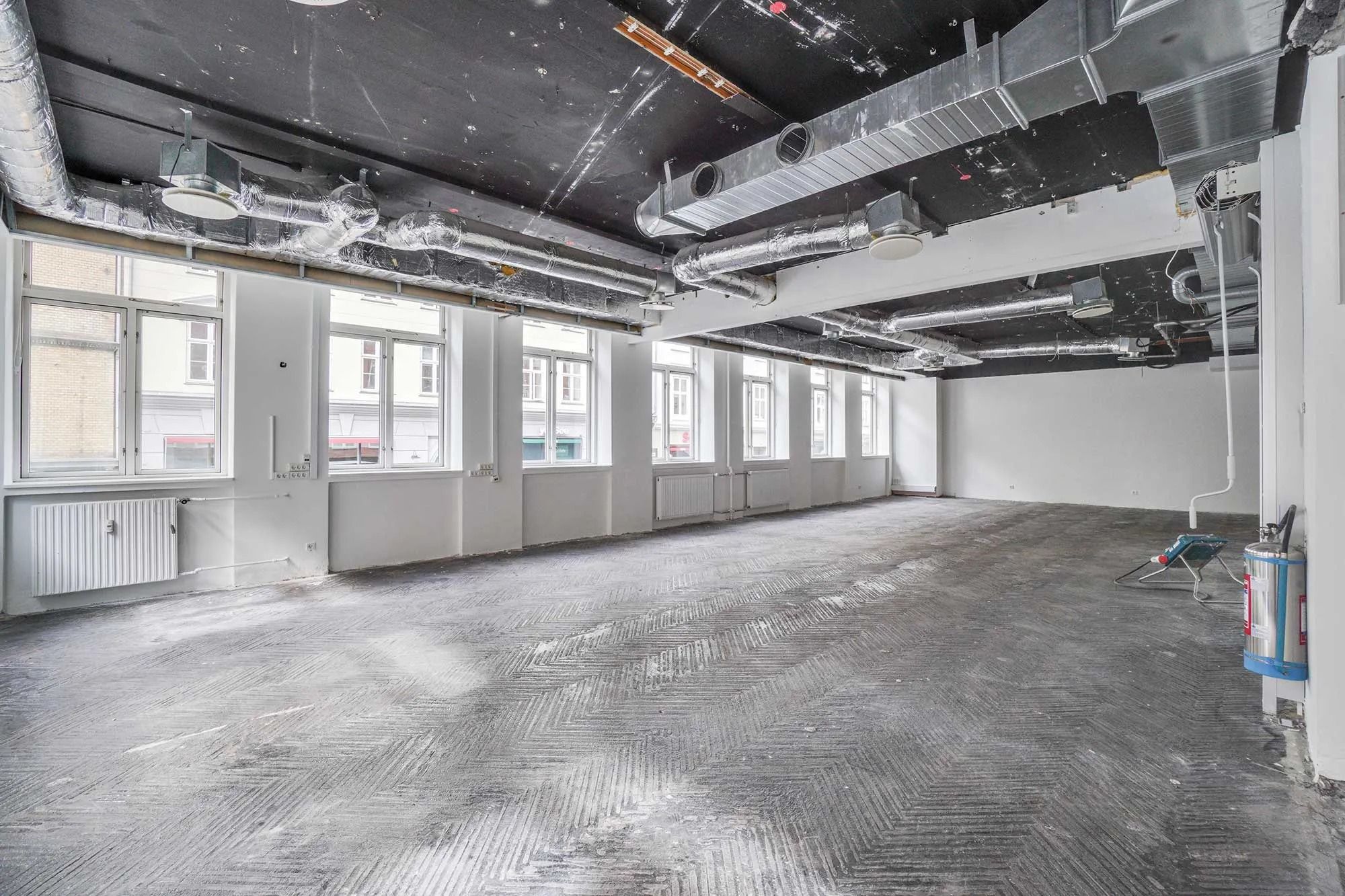Tom lejemål med vinduer og radiatorer. Rør og ventilatorer i loftet. Glatte gulv med mønster og støv.