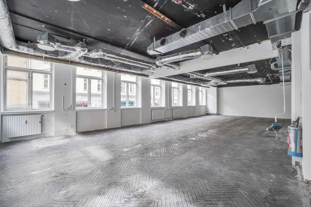 Tom lejemål med vinduer og radiatorer. Rør og ventilatorer i loftet. Glatte gulv med mønster og støv.