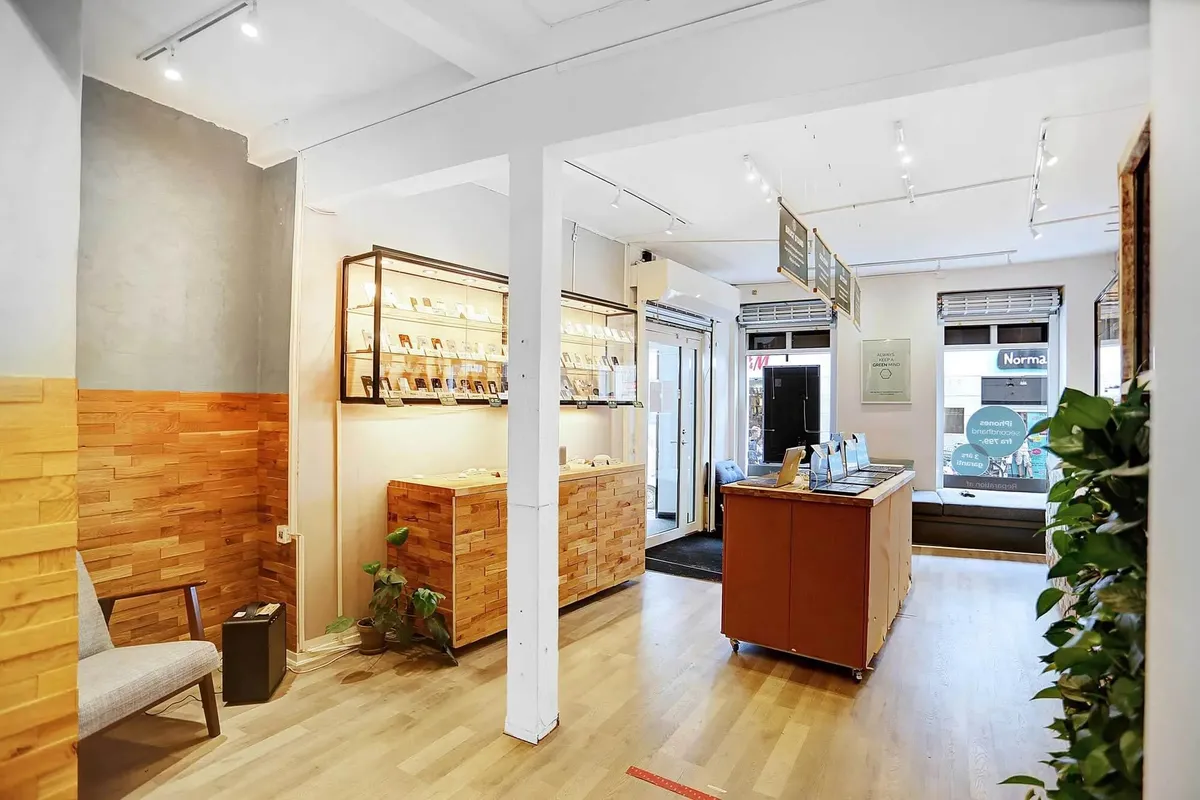 Interiør med lyse trægulve, lyse pletter og møbler. En høj, rusten hylde med genstande og tekster i en hjørne. Der er også