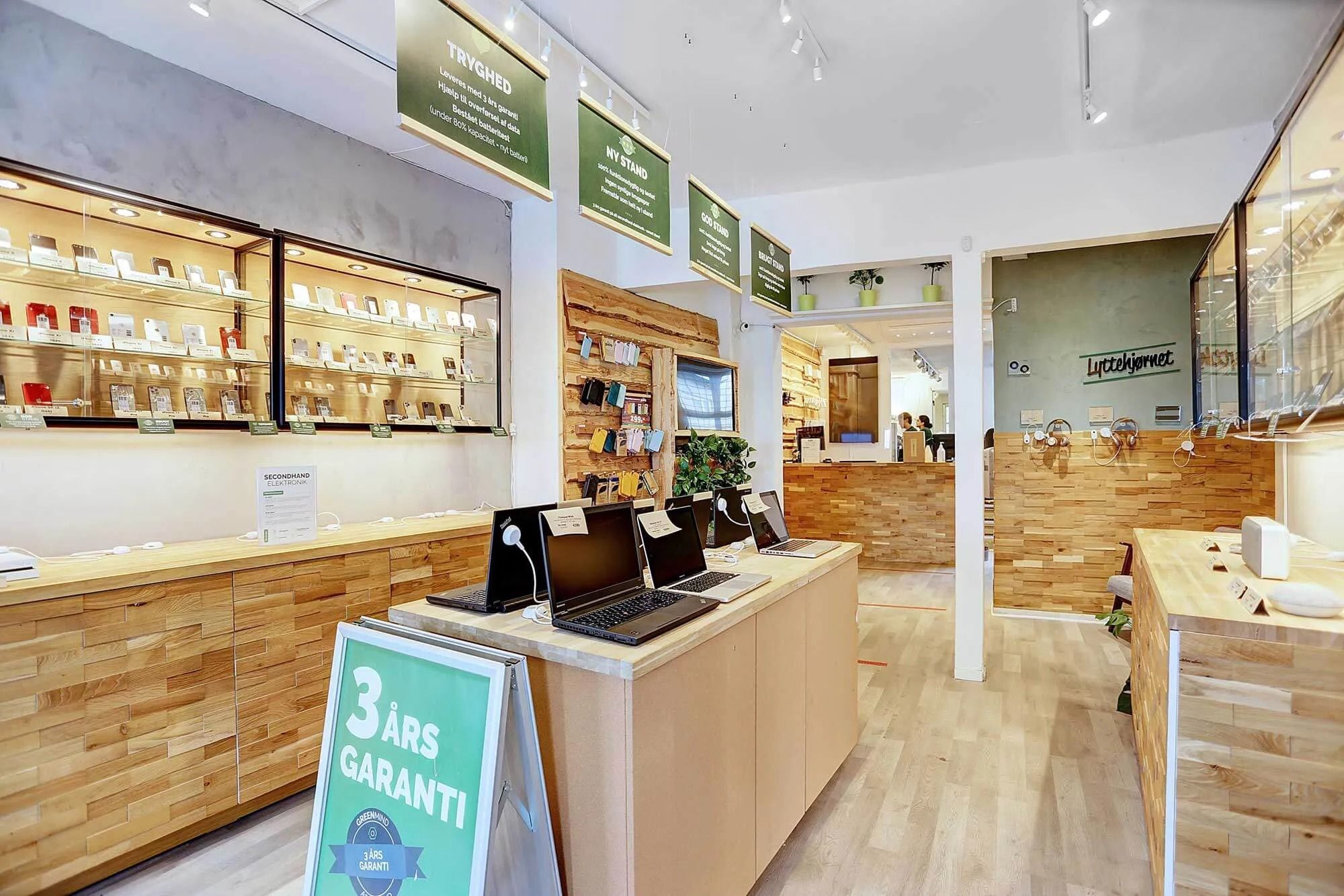 Laptoppe på et salgsbord med et skilt, der står 3 års garanti og butiksreoler med produkter og plantepoter
