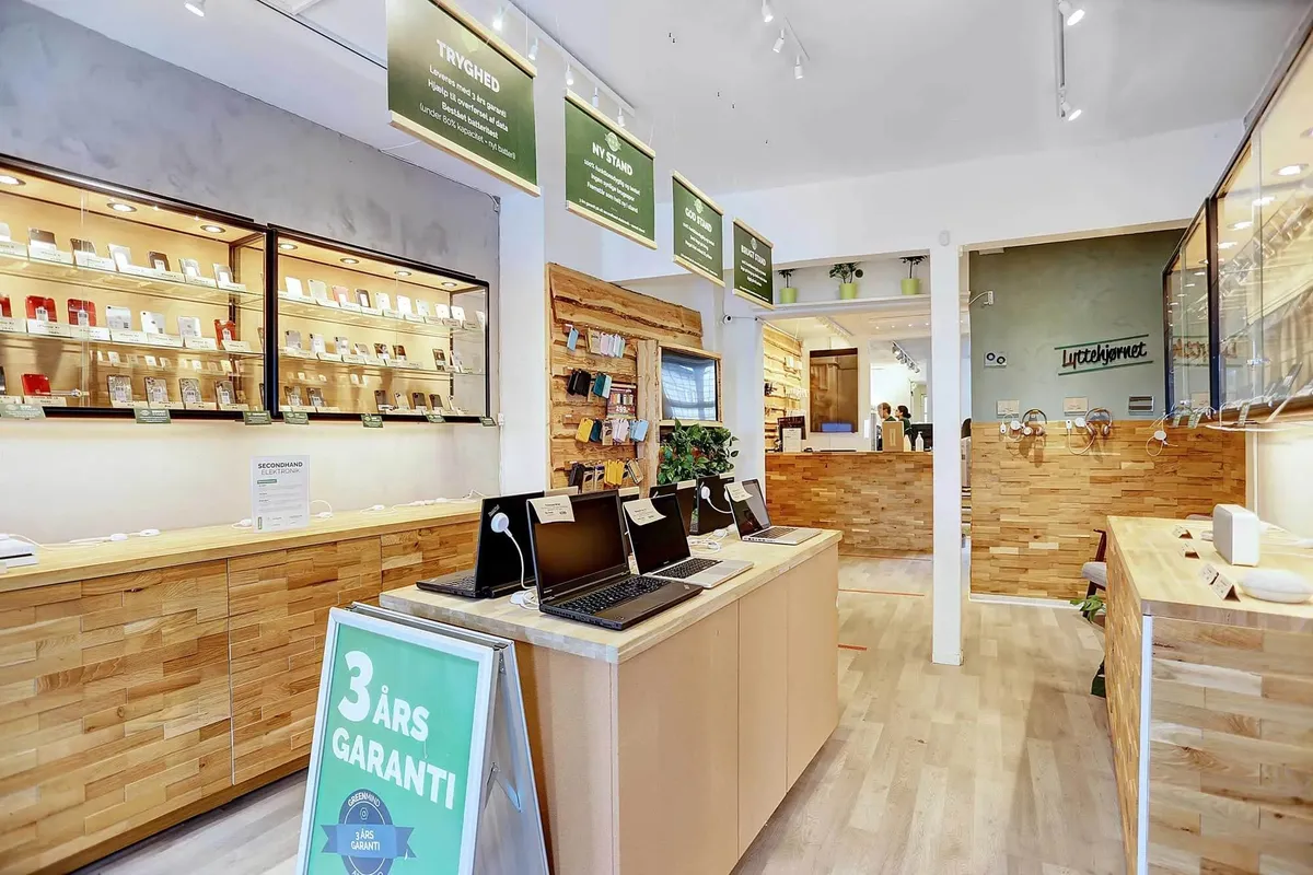 Laptoppe på et salgsbord med et skilt, der står 3 års garanti og butiksreoler med produkter og plantepoter