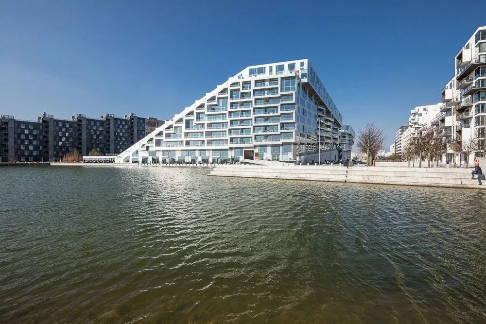 Moderne hvide bygninger med glasvinduer langs vandkanten ud for en vandsamling med søbred