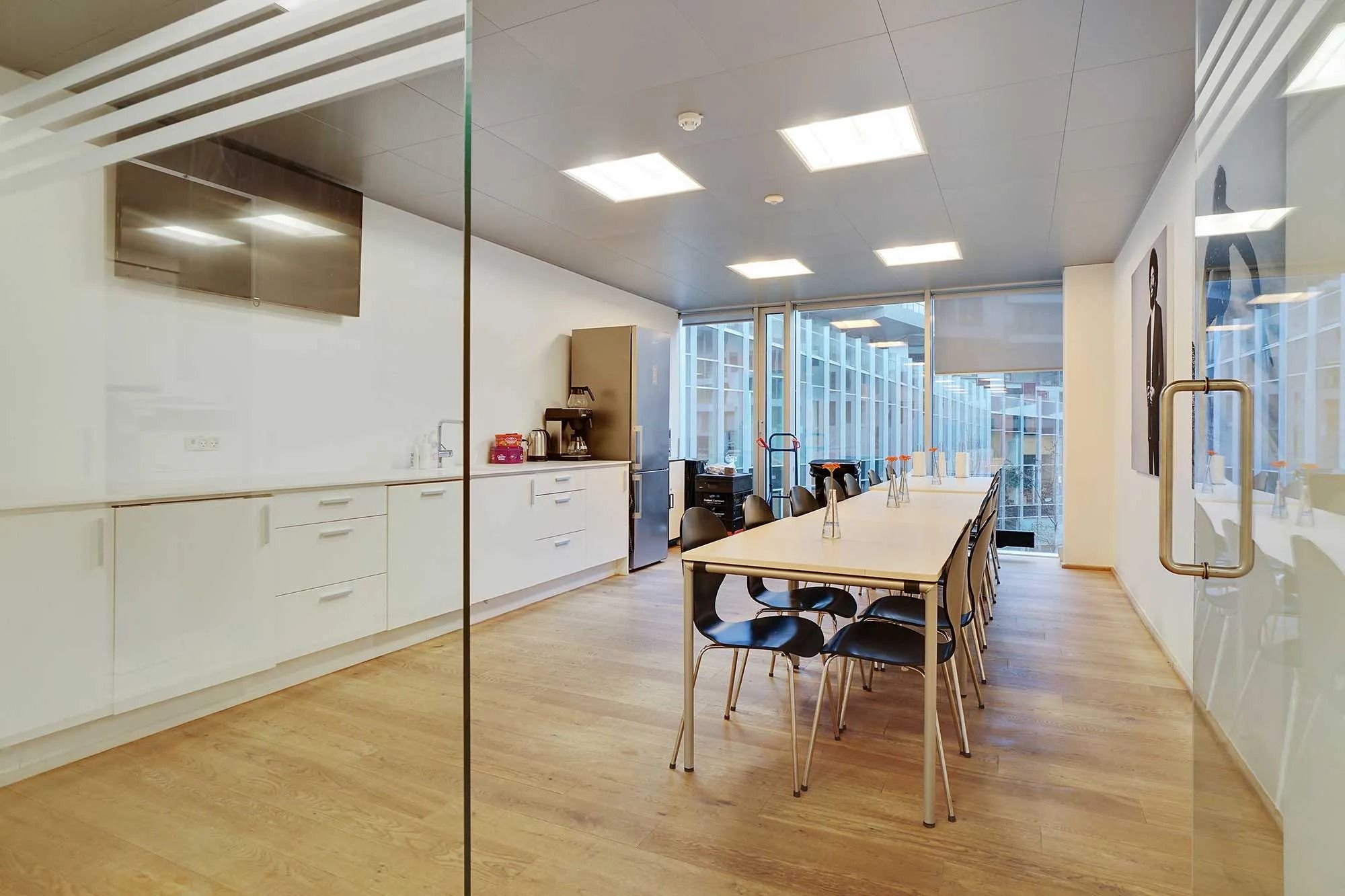 Kontorlejemål med moderne møbler og trægulv, køkken med apparater og kaffemaskine og en terrasse med udsigt til bygninger