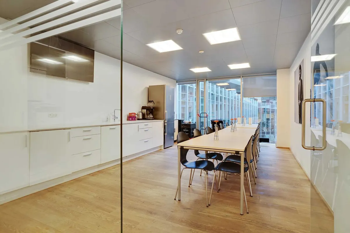 Kontorlejemål med moderne møbler og trægulv, køkken med apparater og kaffemaskine og en terrasse med udsigt til bygninger