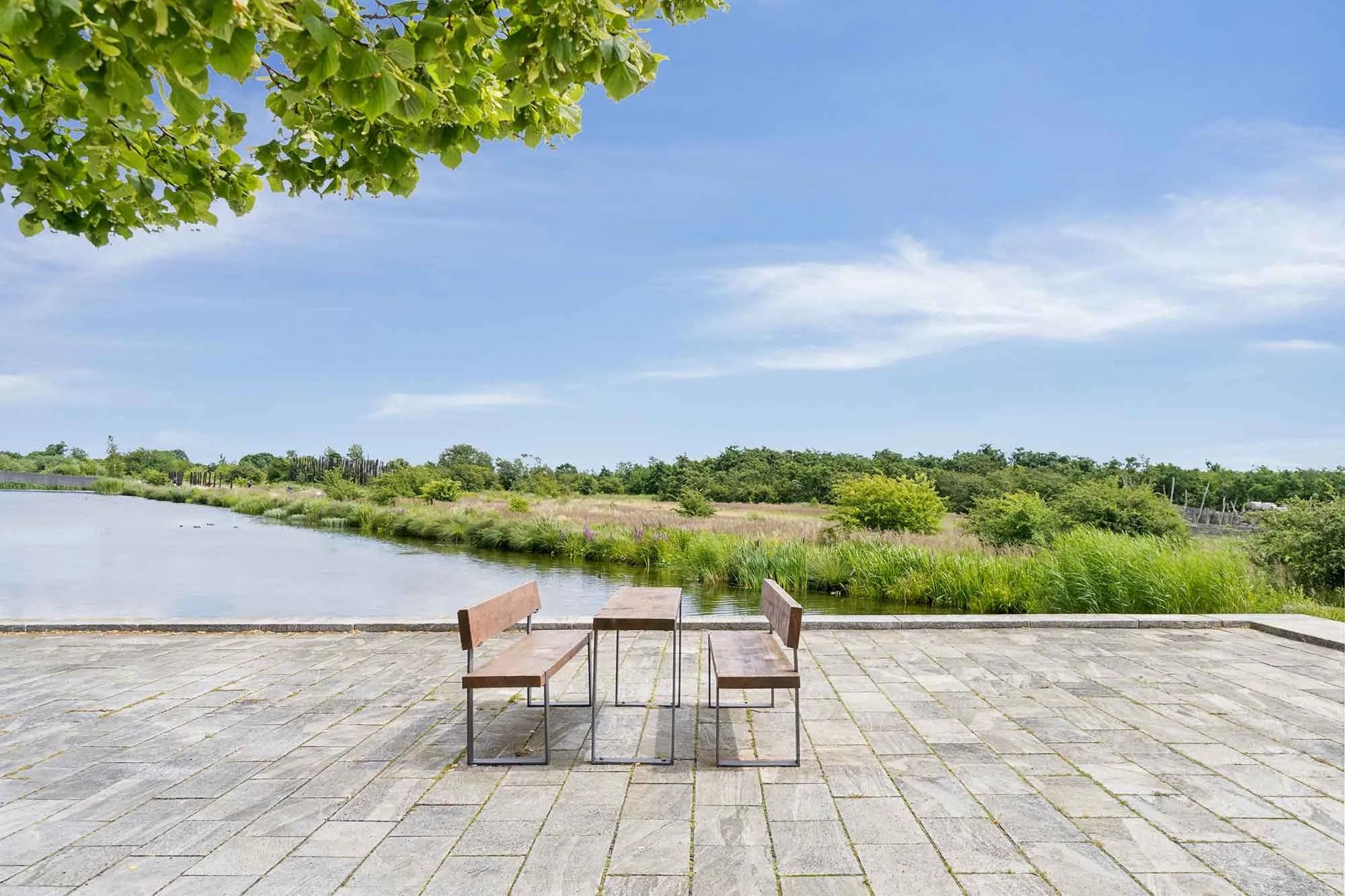 To bænke og et bord står på en terrasse med udsigt over en sø og landskabet