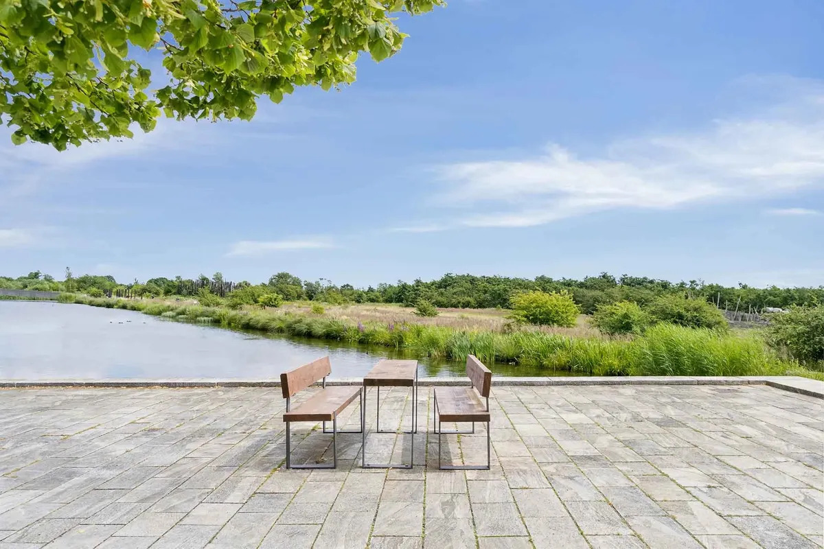 To bænke og et bord står på en terrasse med udsigt over en sø og landskabet