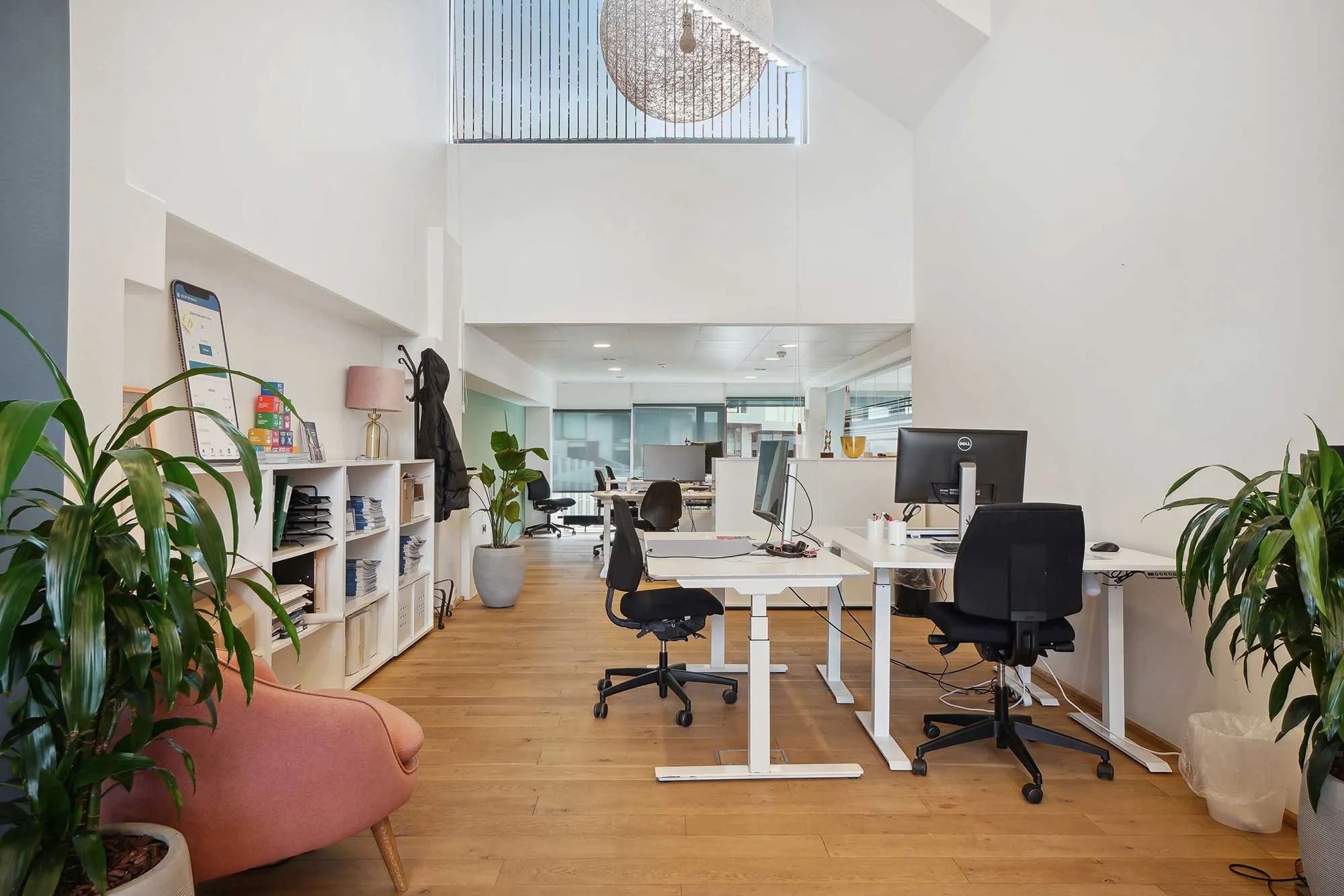 Kontor med moderne design, højloft, lysegul gulv, hvide vægge, skriveborde og stolpe. Planter og møbler for at skabe en