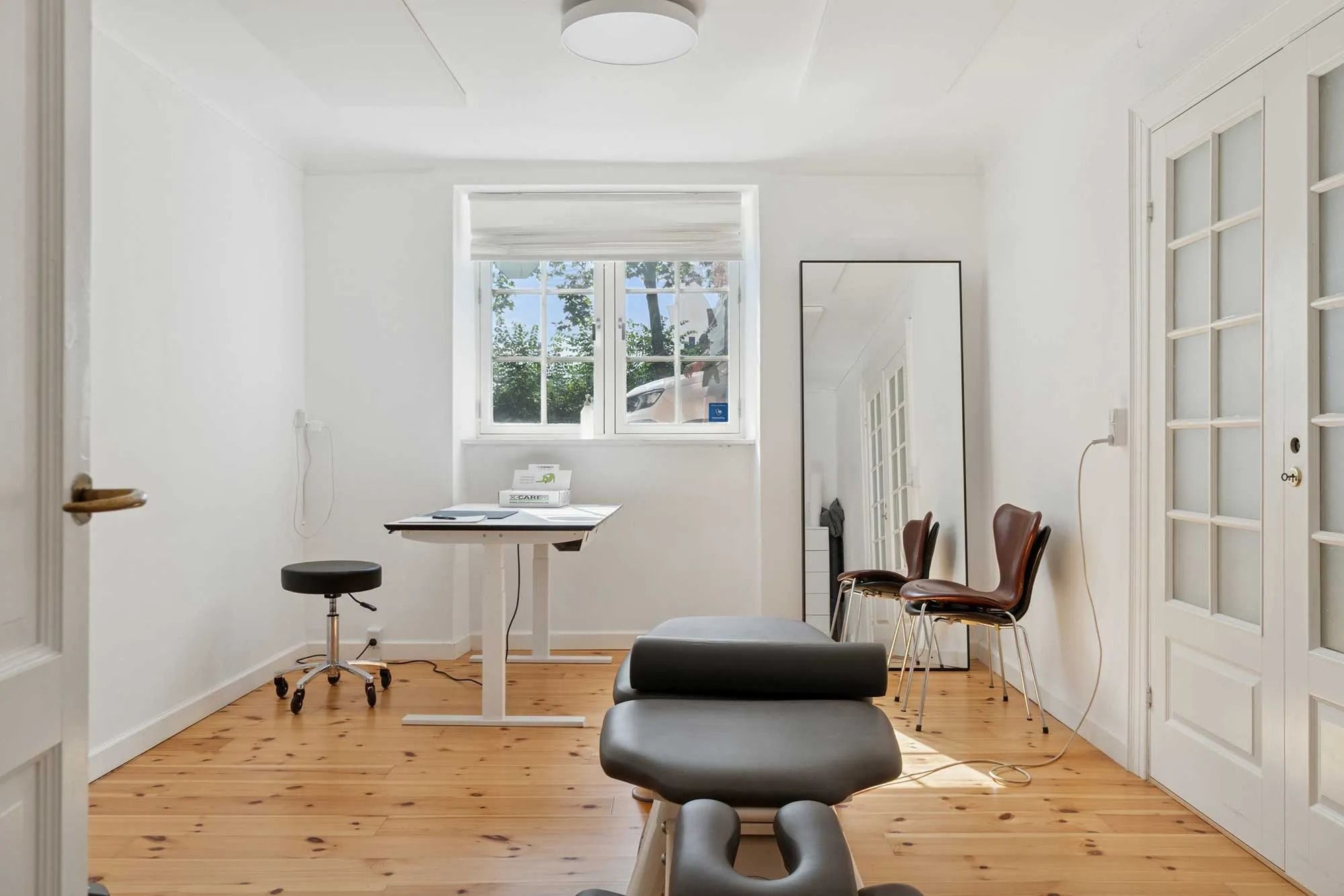 Kontor med højt loft, lysegul gulv og lysegrå vægge med en stor spejl og en skrivebord i et stille og soligt rum